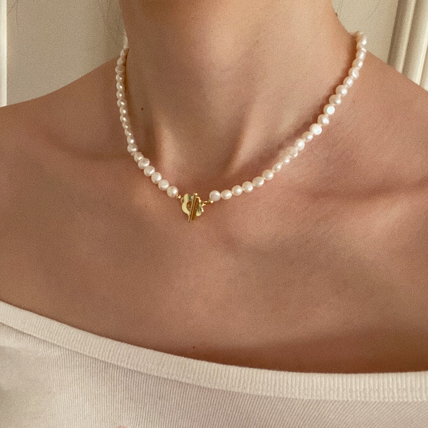 Model wearing short freshwater pearl choker with gold flower toggle clasp on bare collarbone
