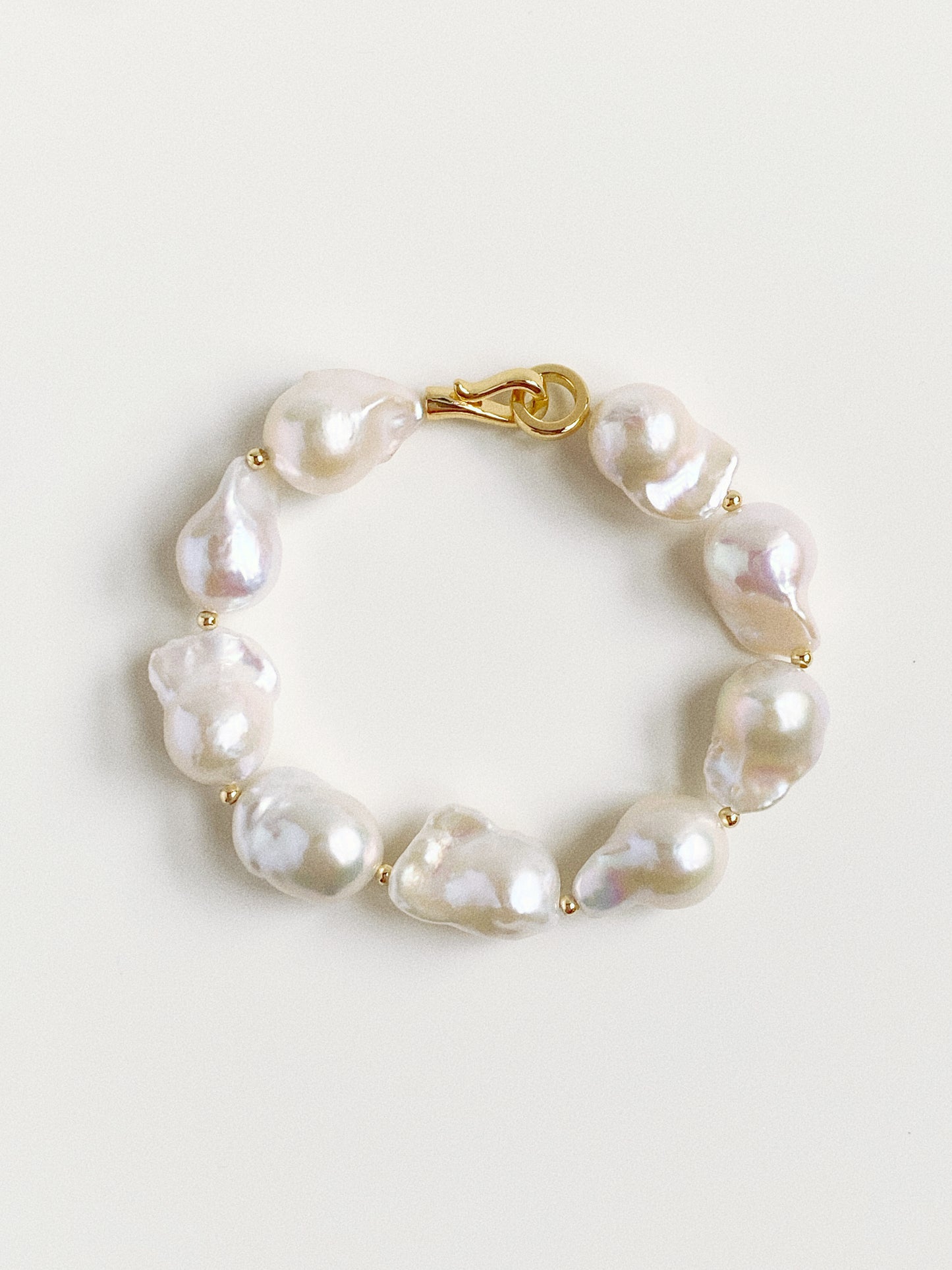 Flat lay of a large baroque pearl bracelet featuring 11-13mm fish-tail pearls and a gold S-hook clasp.