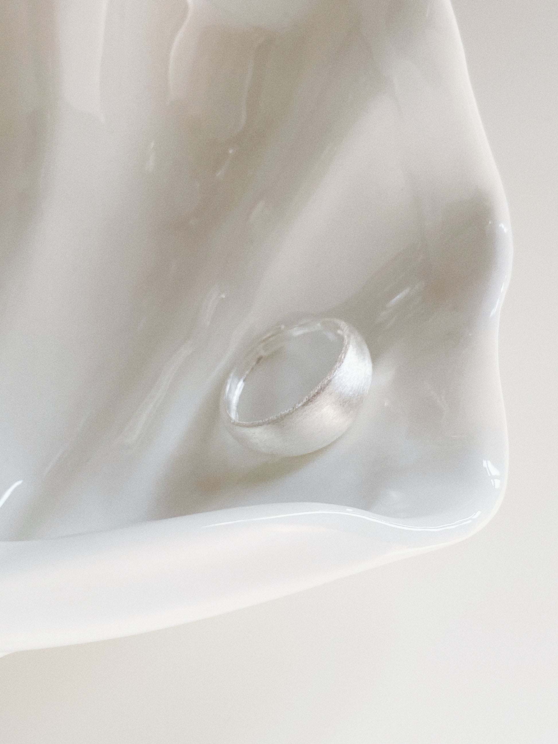 A chunky silver dome ring with a satin matte texture placed inside a white decorative shell tray.