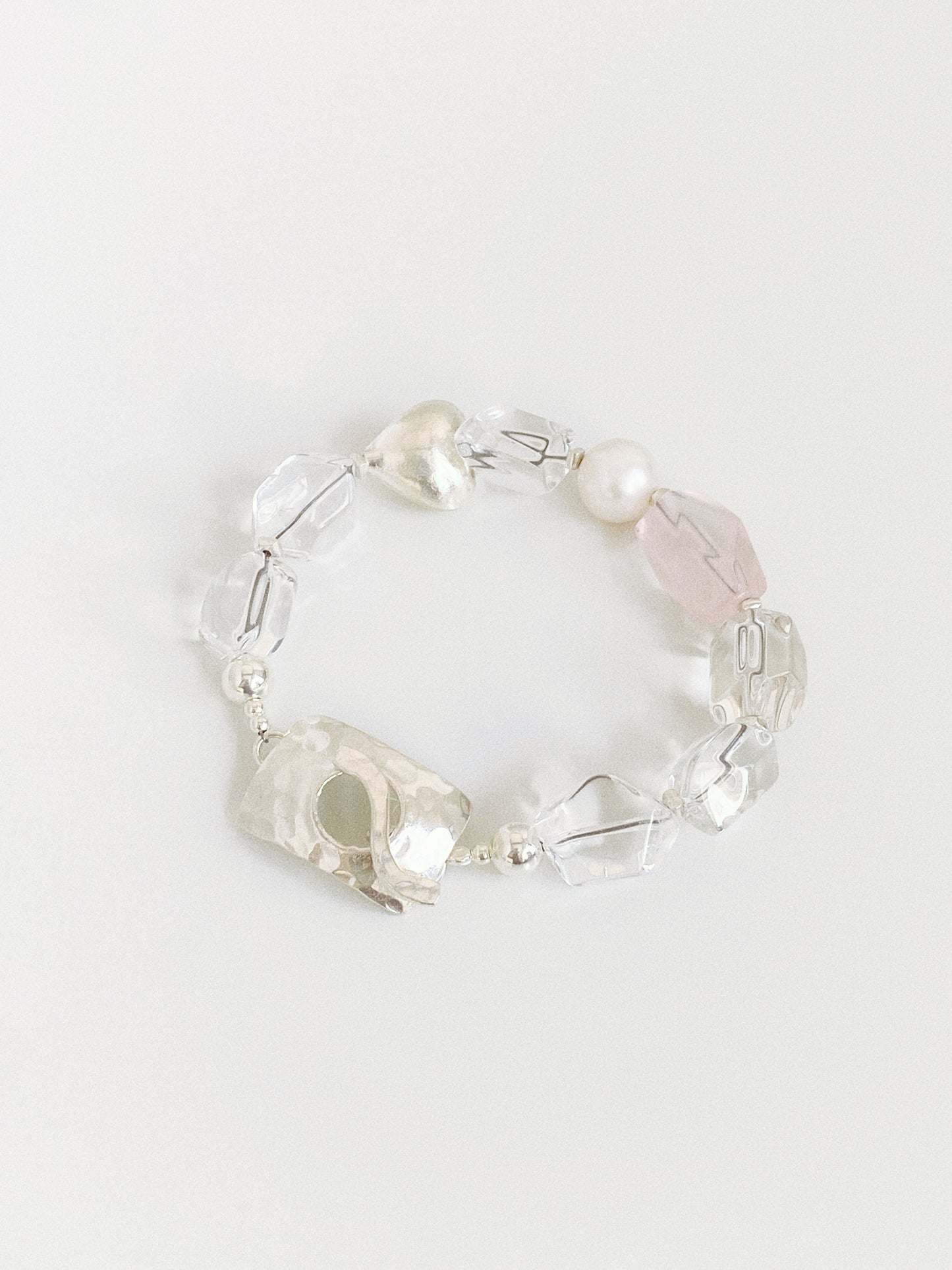 Flat lay of a natural clear quartz and rose quartz bracelet with pearl and hammered sterling silver toggle clasp on white