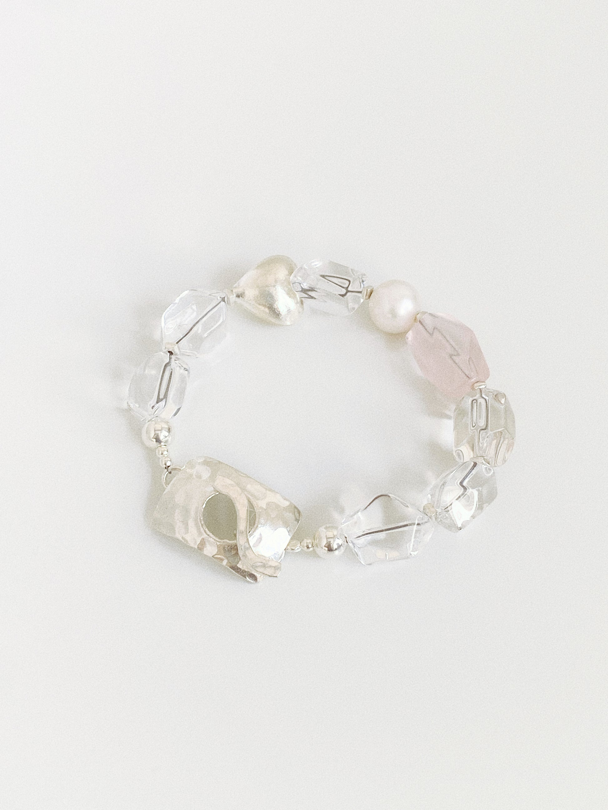 Flat lay of a natural clear quartz and rose quartz bracelet with pearl and hammered sterling silver toggle clasp on white