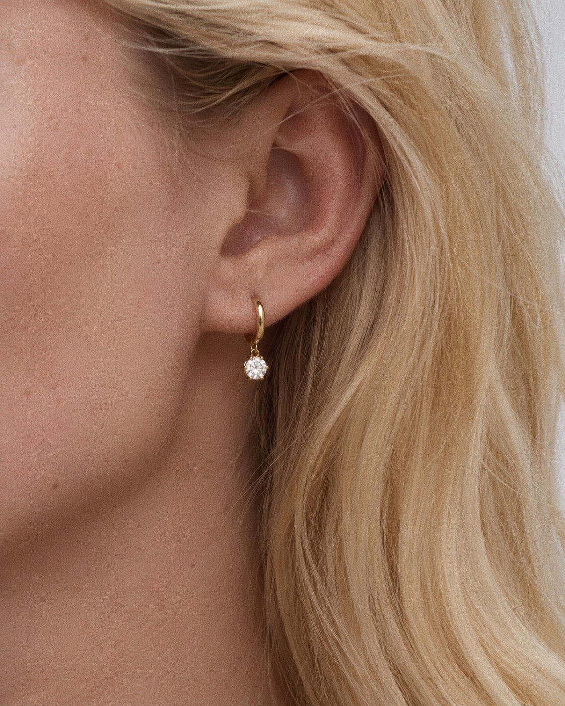 Model wearing the Icon huggie hoop earring with the round cz solitaire swinging just below the lobe