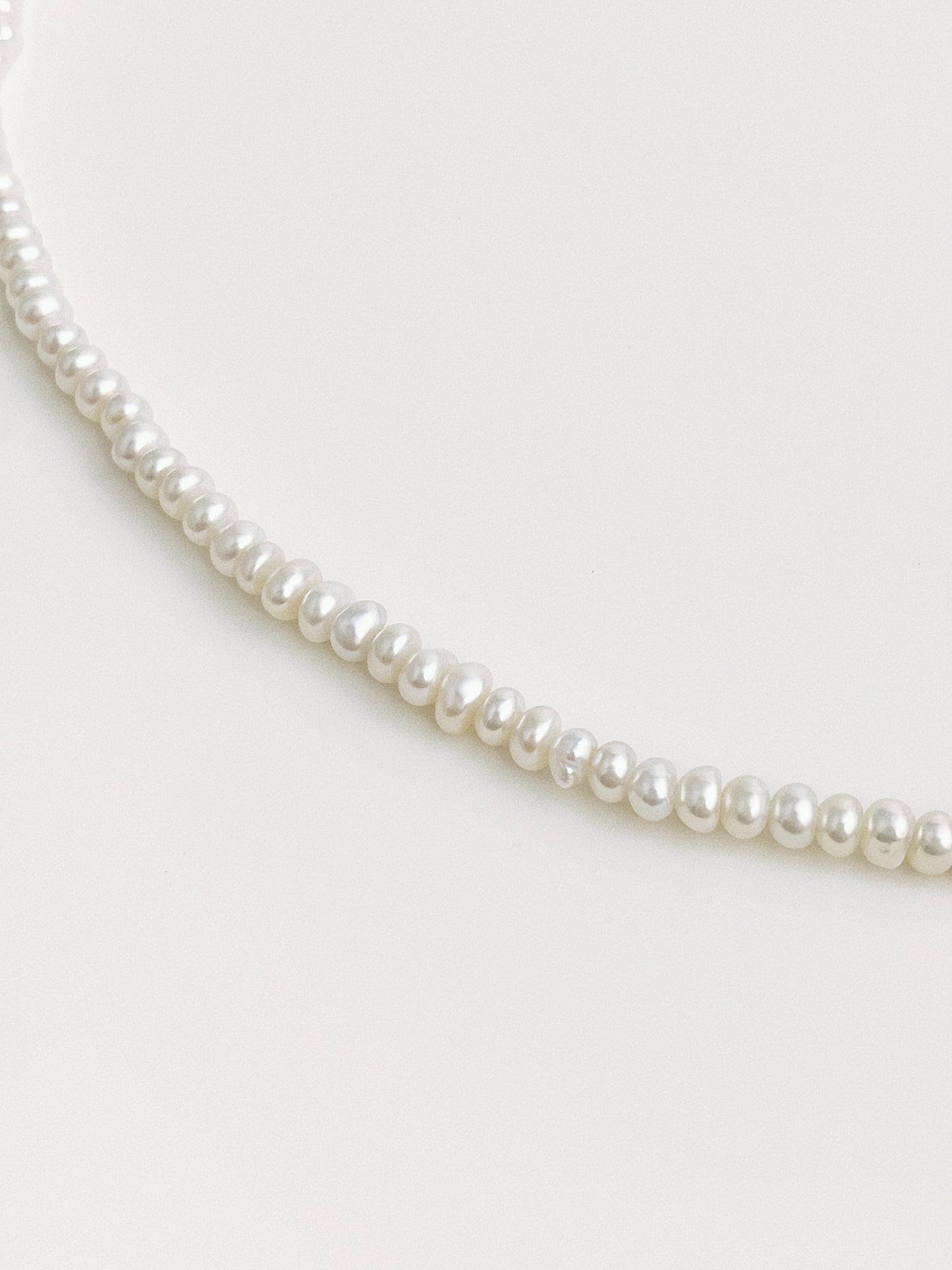 Close-up of dainty button-shape freshwater pearls strung as fine choker necklace
