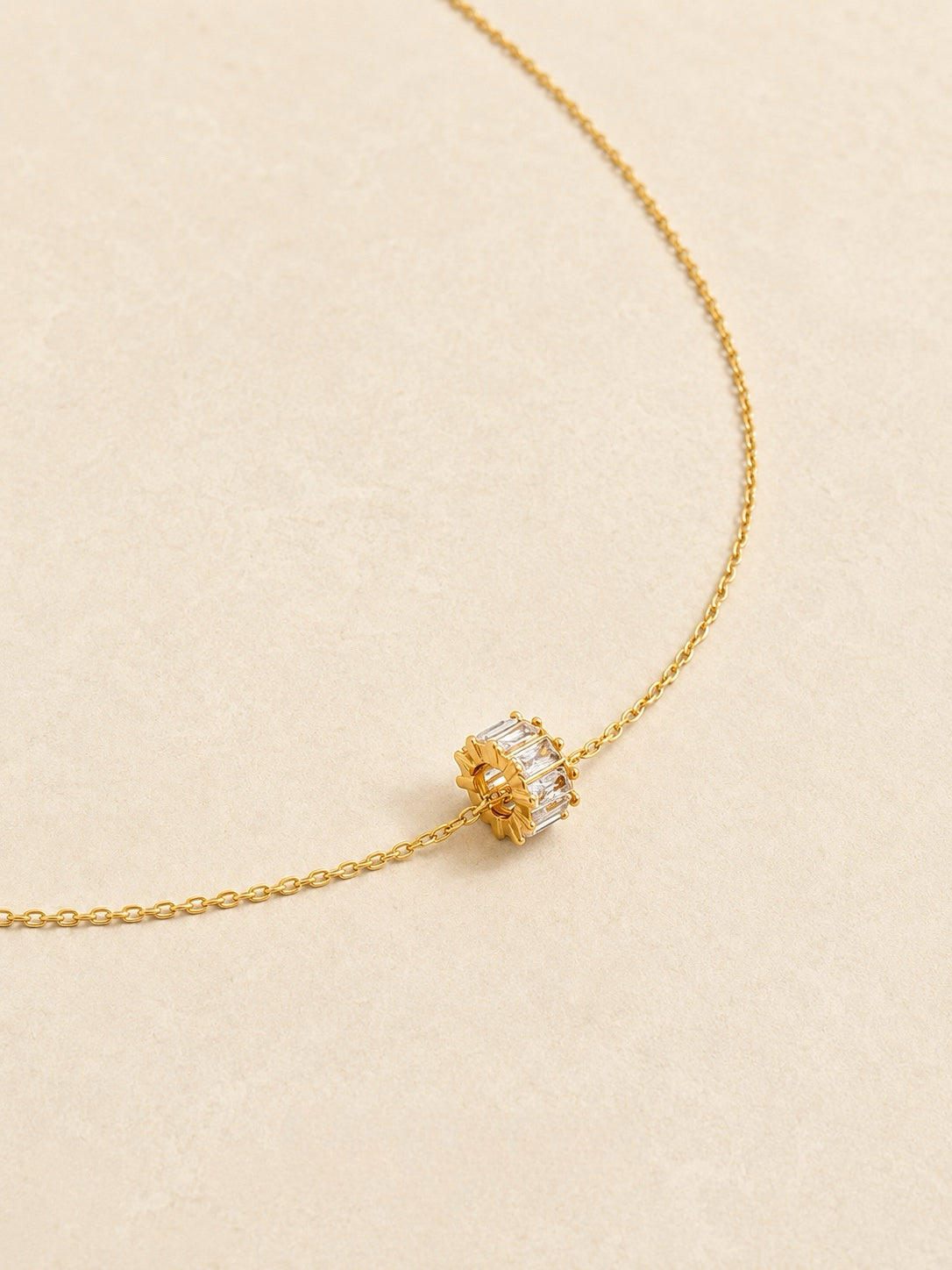 Angled view of a fine gold cable chain necklace with a small barrel-shaped baguette cubic zirconia wheel charm