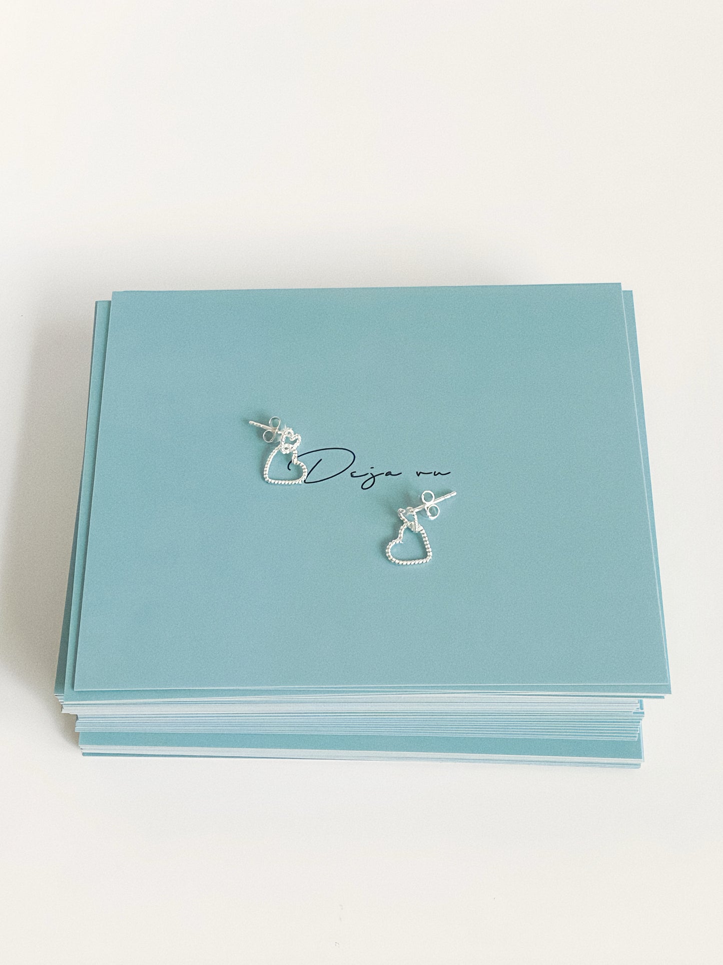 Dainty silver double heart stud earrings shown with sterling silver posts on Deja Vu Jewellery branded packaging