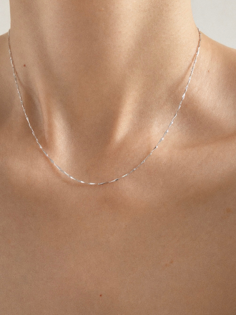Close view of a fine 925 sterling silver bar chain necklace resting along the collarbone on bare skin