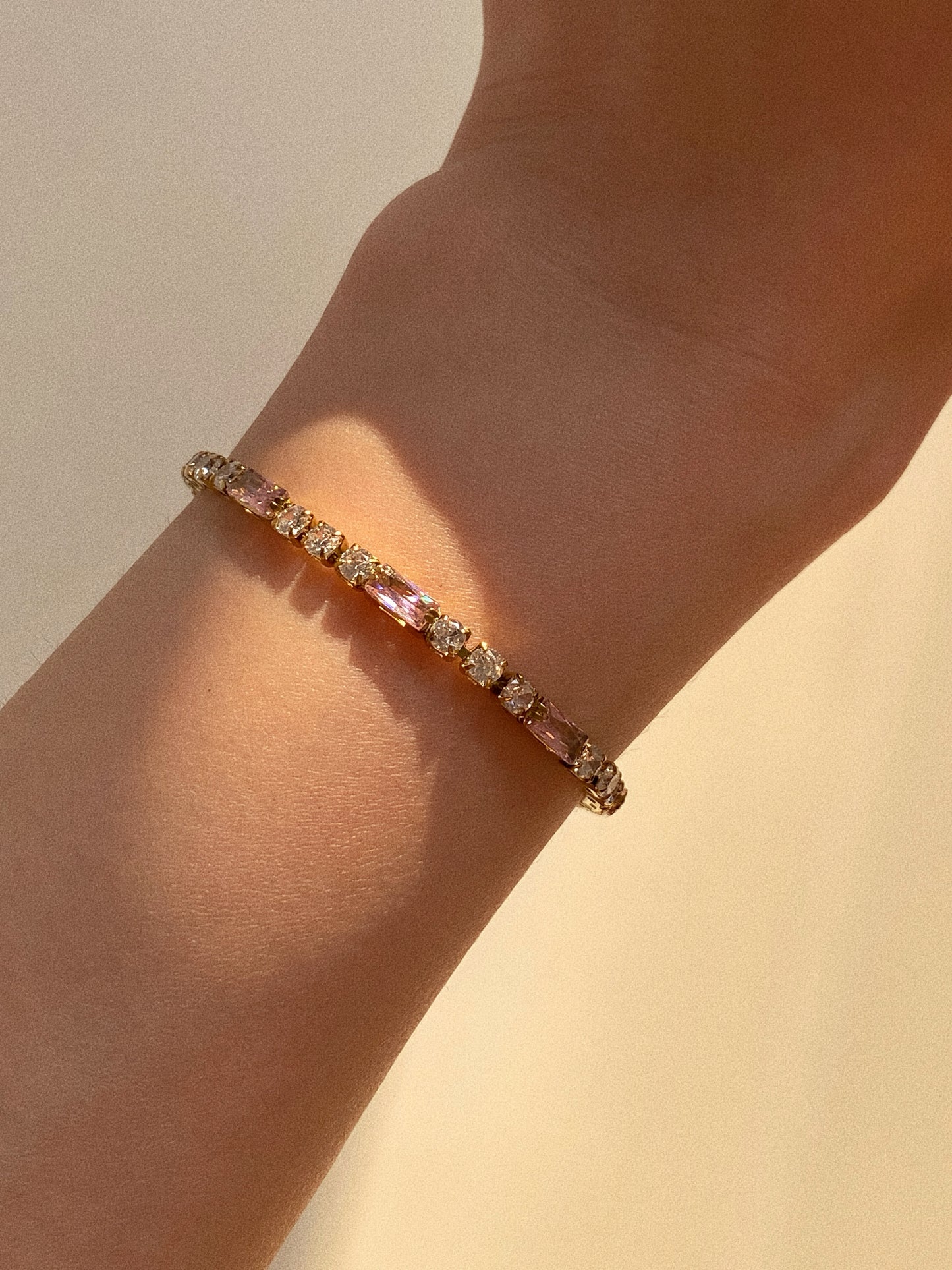 Model wearing pink baguette tennis bracelet, 16cm petite fit on wrist, aesthetic golden hour lighting.