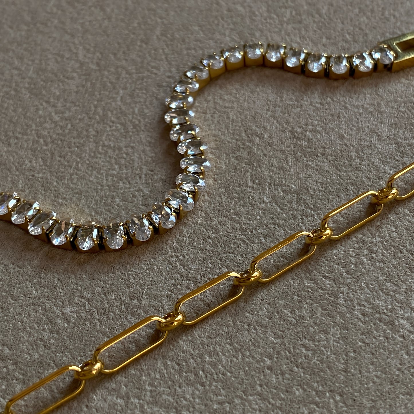 Macro of gold Oval CZ Tennis Bracelet next to a paperclip chain—oval-cut cubic zirconia prong set for maximum sparkle.