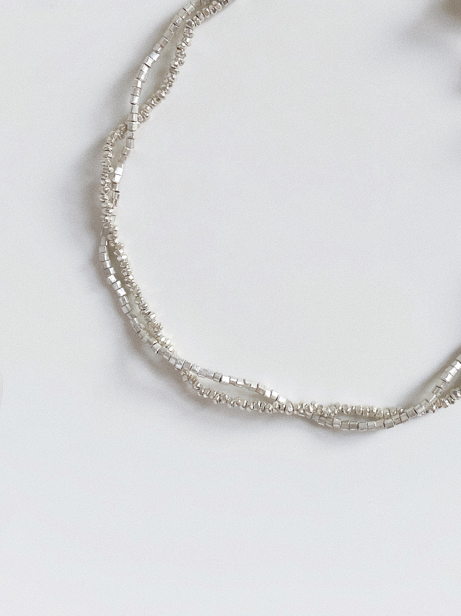 Macro shot of faceted silver beads and crushed silver texture on a dainty layered bracelet.