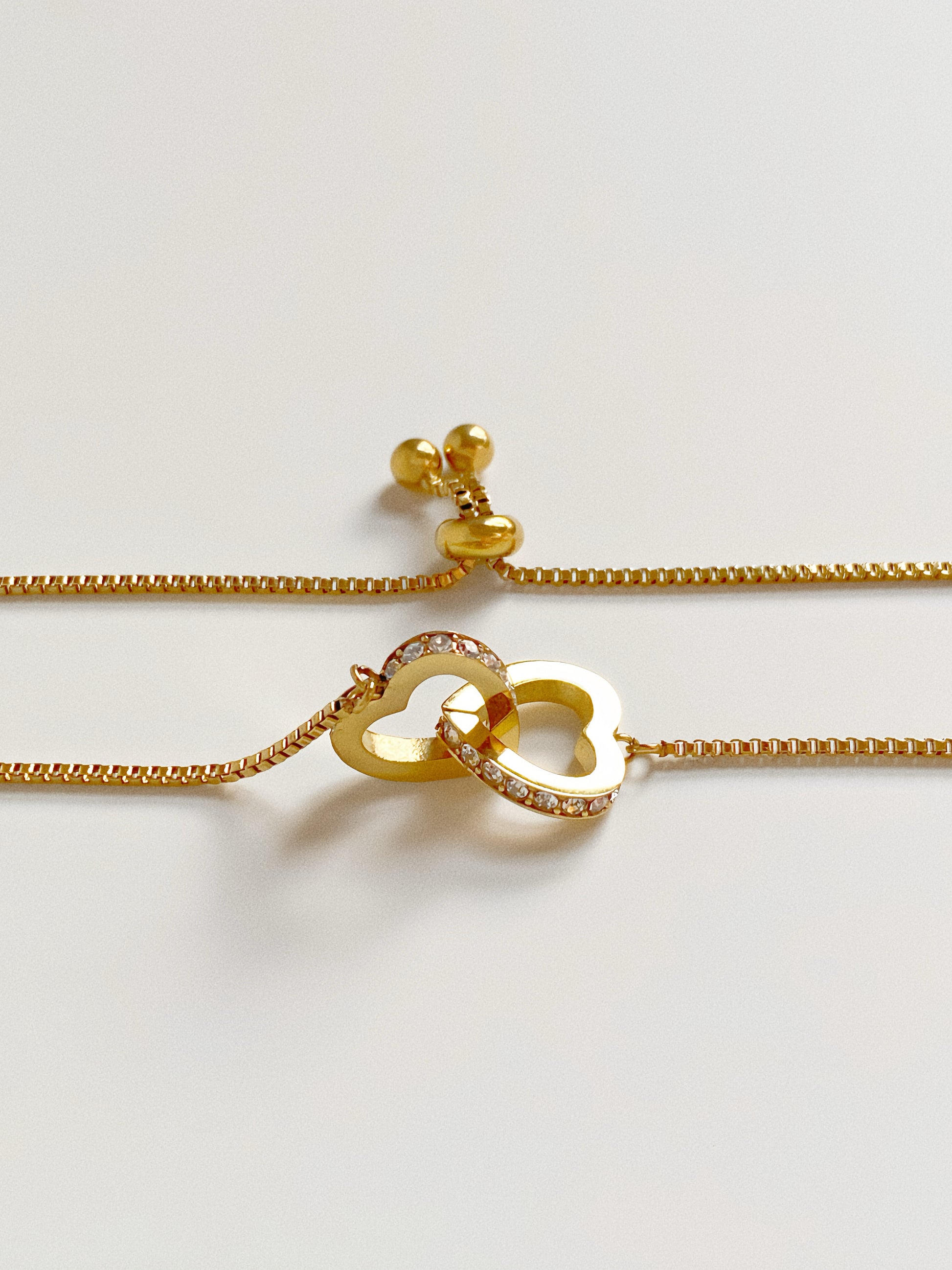 Close up of adjustable slider clasp mechanism on a gold box chain bracelet with heart charms.