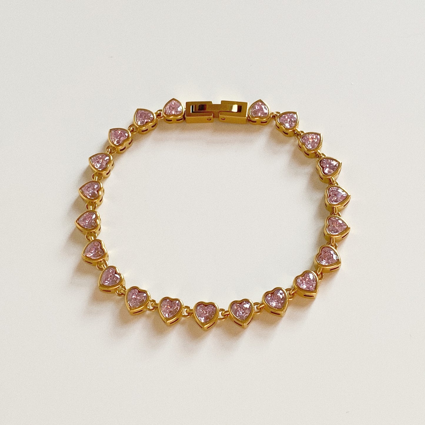 Isolated shot of pink heart tennis bracelet showing secure gold clasp mechanism and stainless steel construction.