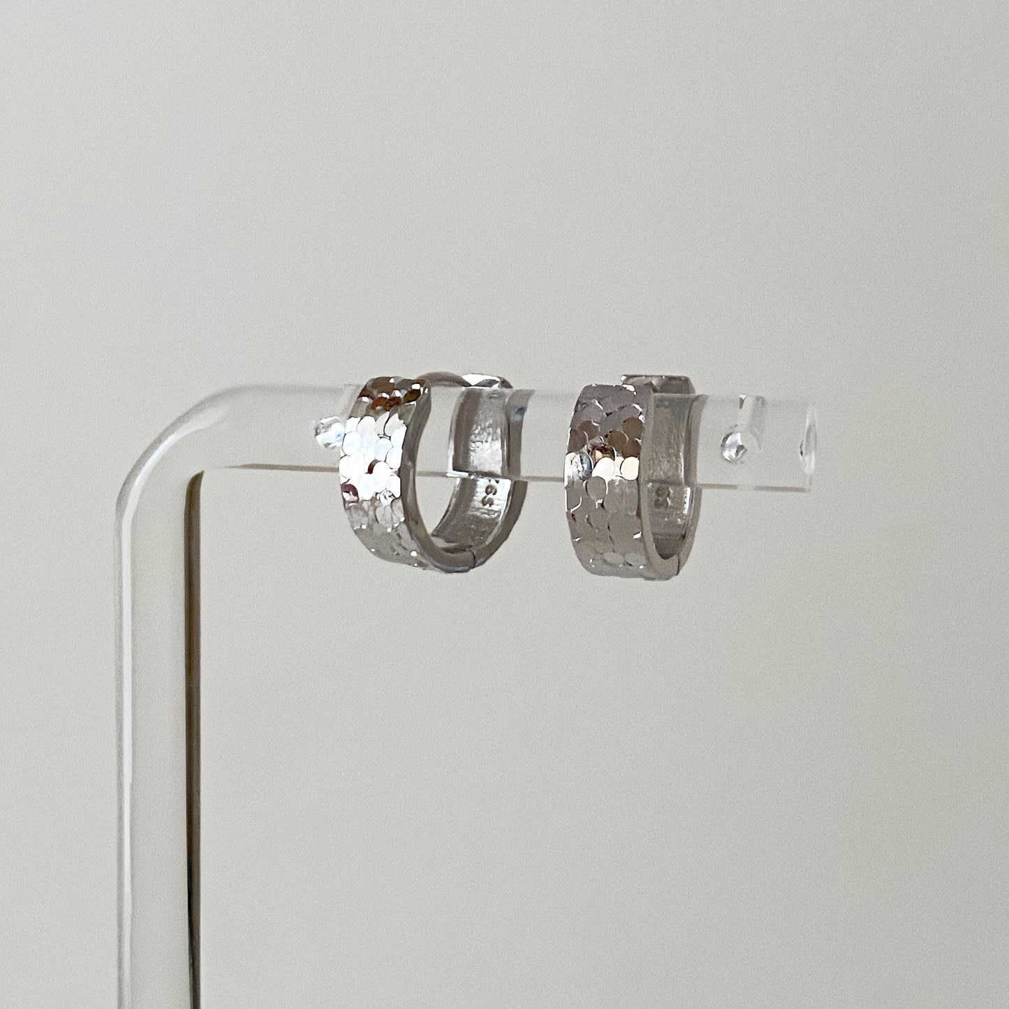 Close up of hammered silver hoop earrings showing the light-reflecting scale texture and clicker clasp.