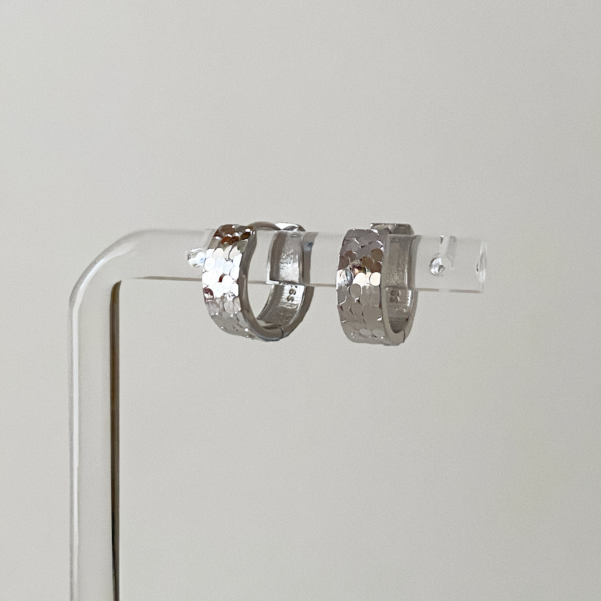 Close up of hammered silver hoop earrings showing the light-reflecting scale texture and clicker clasp.