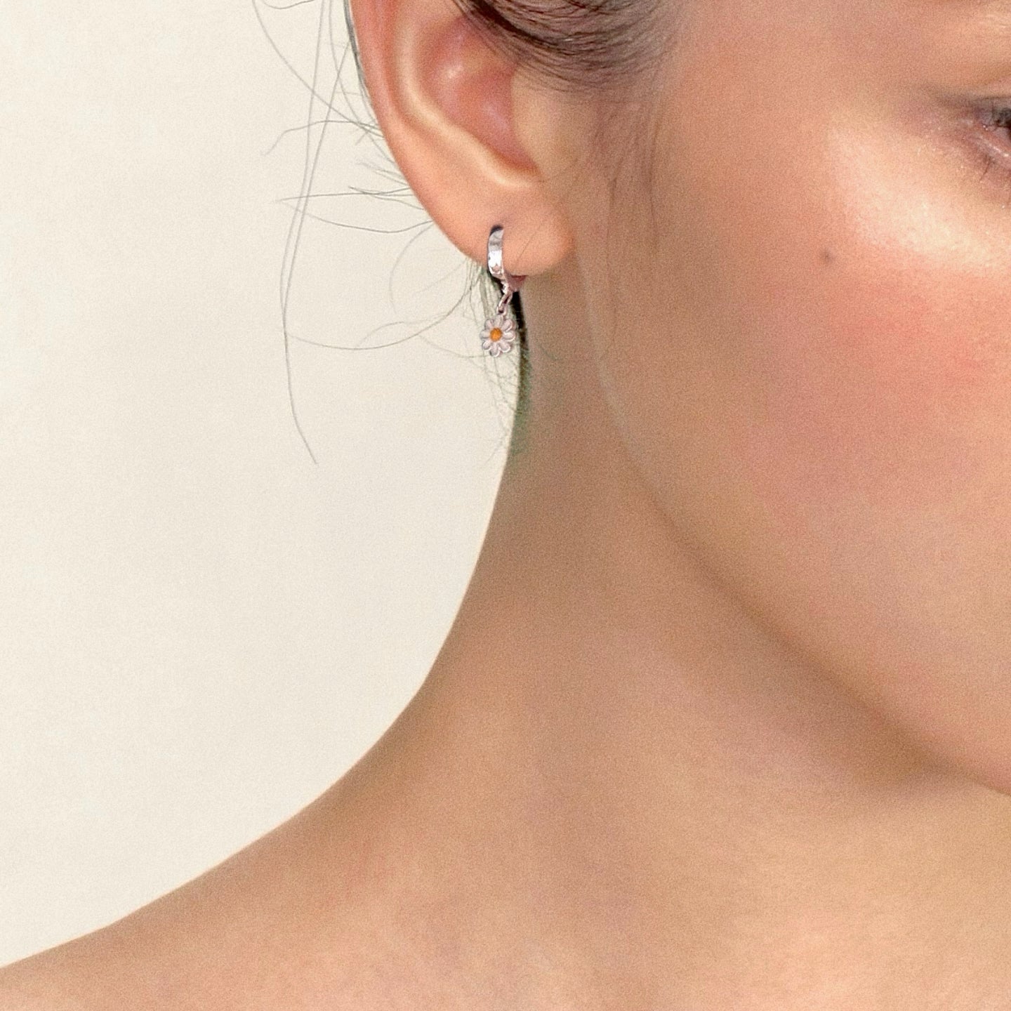 Model wearing tiny sterling-silver daisy huggie hoop earring with enamel charm
