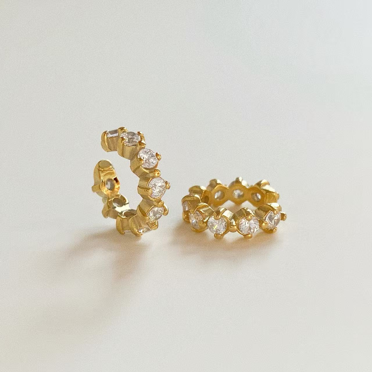 Pair of gold eternity ear cuffs featuring round cubic zirconia crystals, no piercing required.