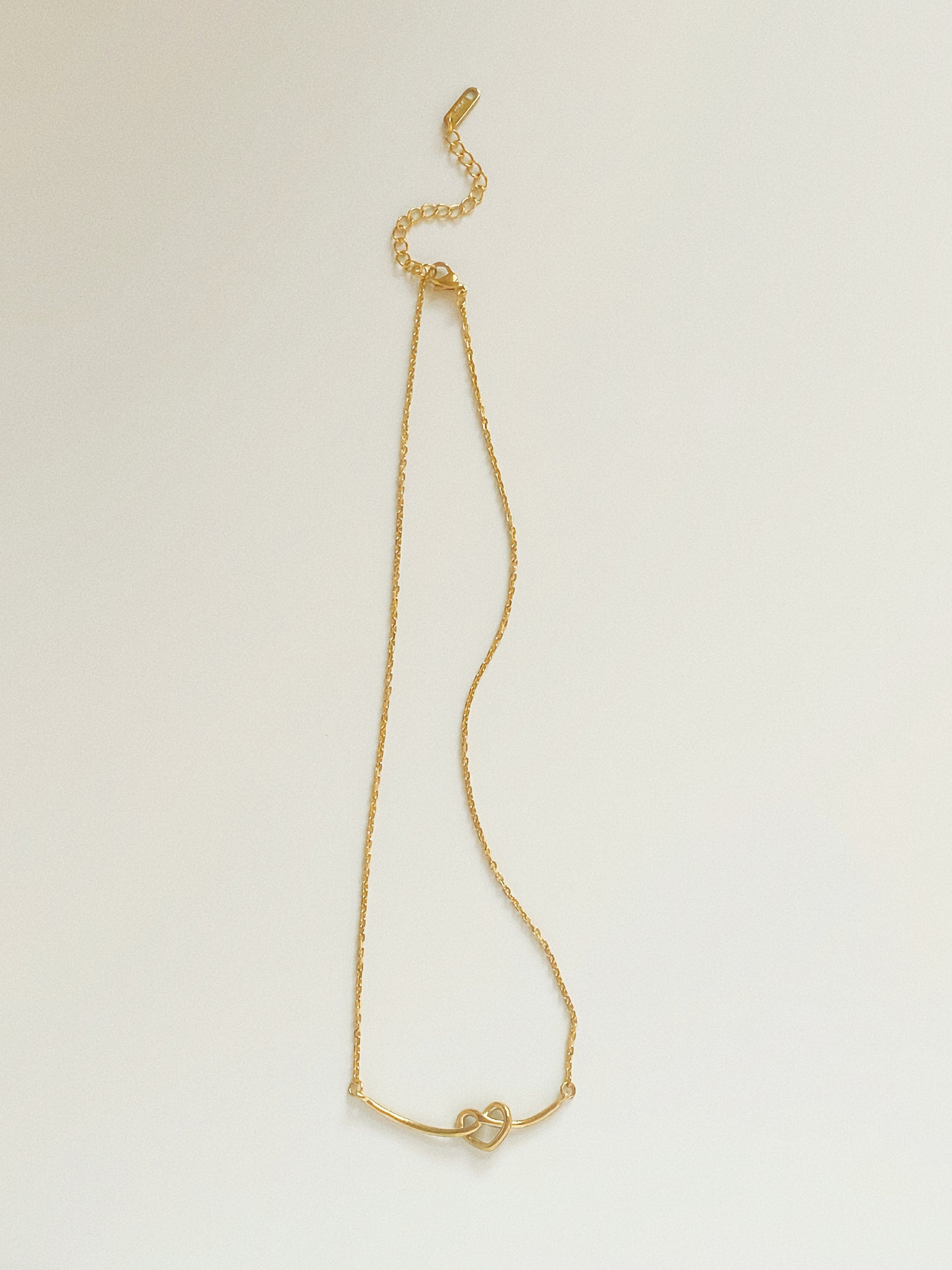 Full length view of gold knot heart smile necklace showing dainty cable chain and adjustable extender.