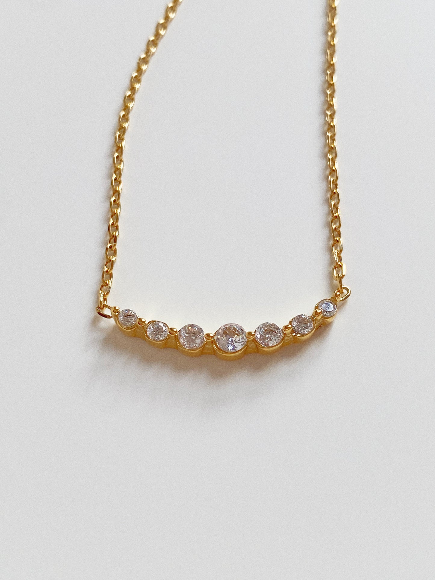 Close up of gold smile necklace featuring a curved bar of seven graduated cubic zirconia crystals.