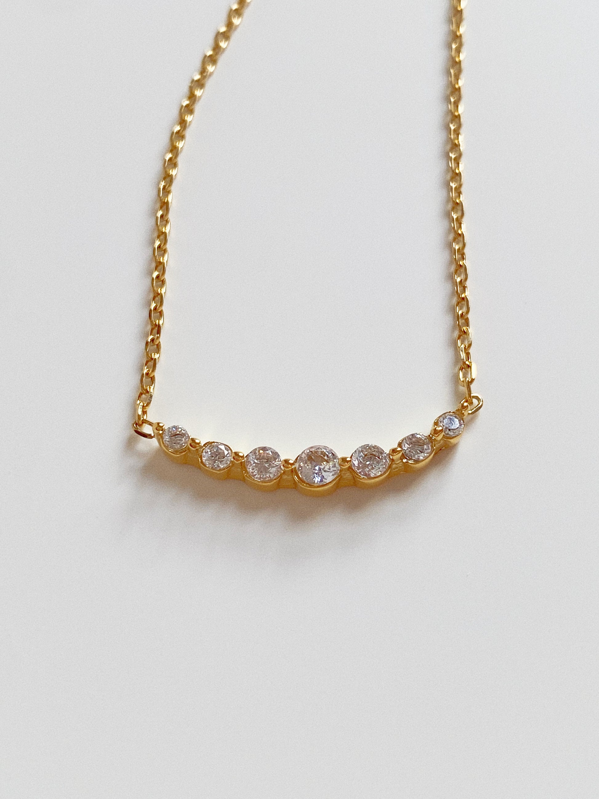 Close up of gold smile necklace featuring a curved bar of seven graduated cubic zirconia crystals.