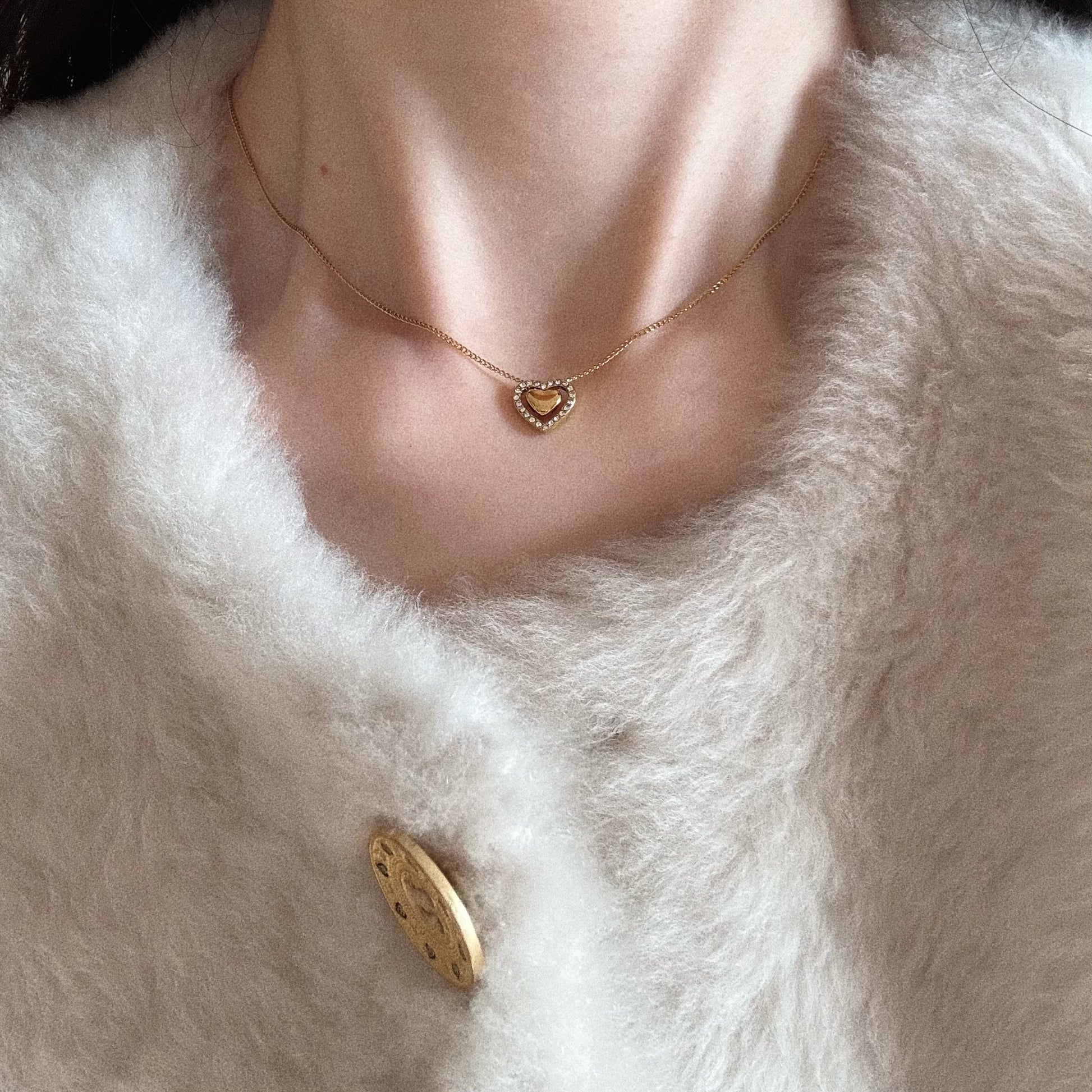 Woman wearing a dainty gold heart-within-a-heart necklace, styled for a romantic everyday look.