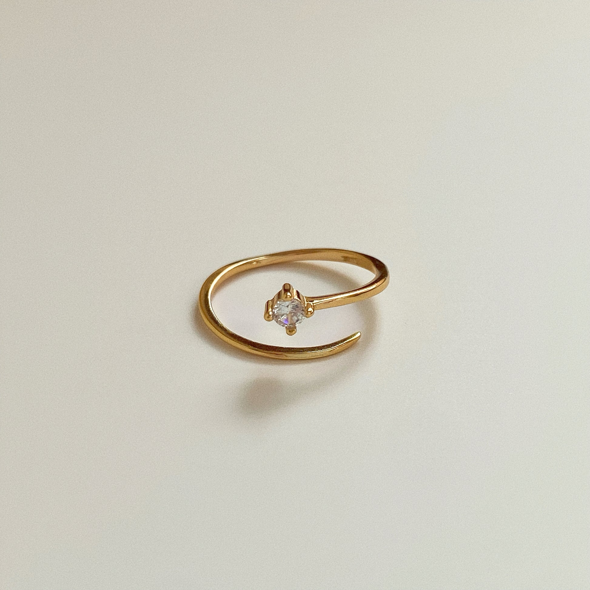 Dainty 18k gold plated sterling silver pinky ring with one cubic zirconia in claw setting on neutral background