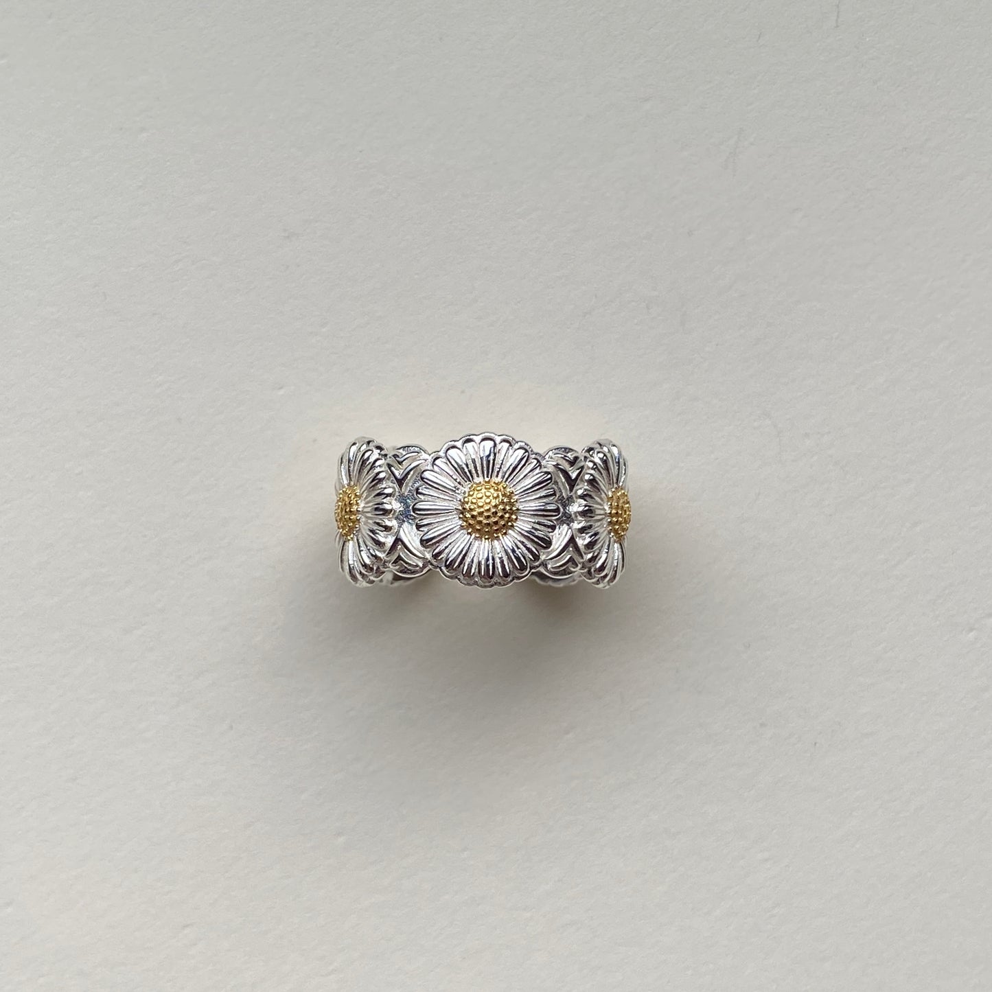 close-up of engraved daisy petals with gold-tone centres on silver ring