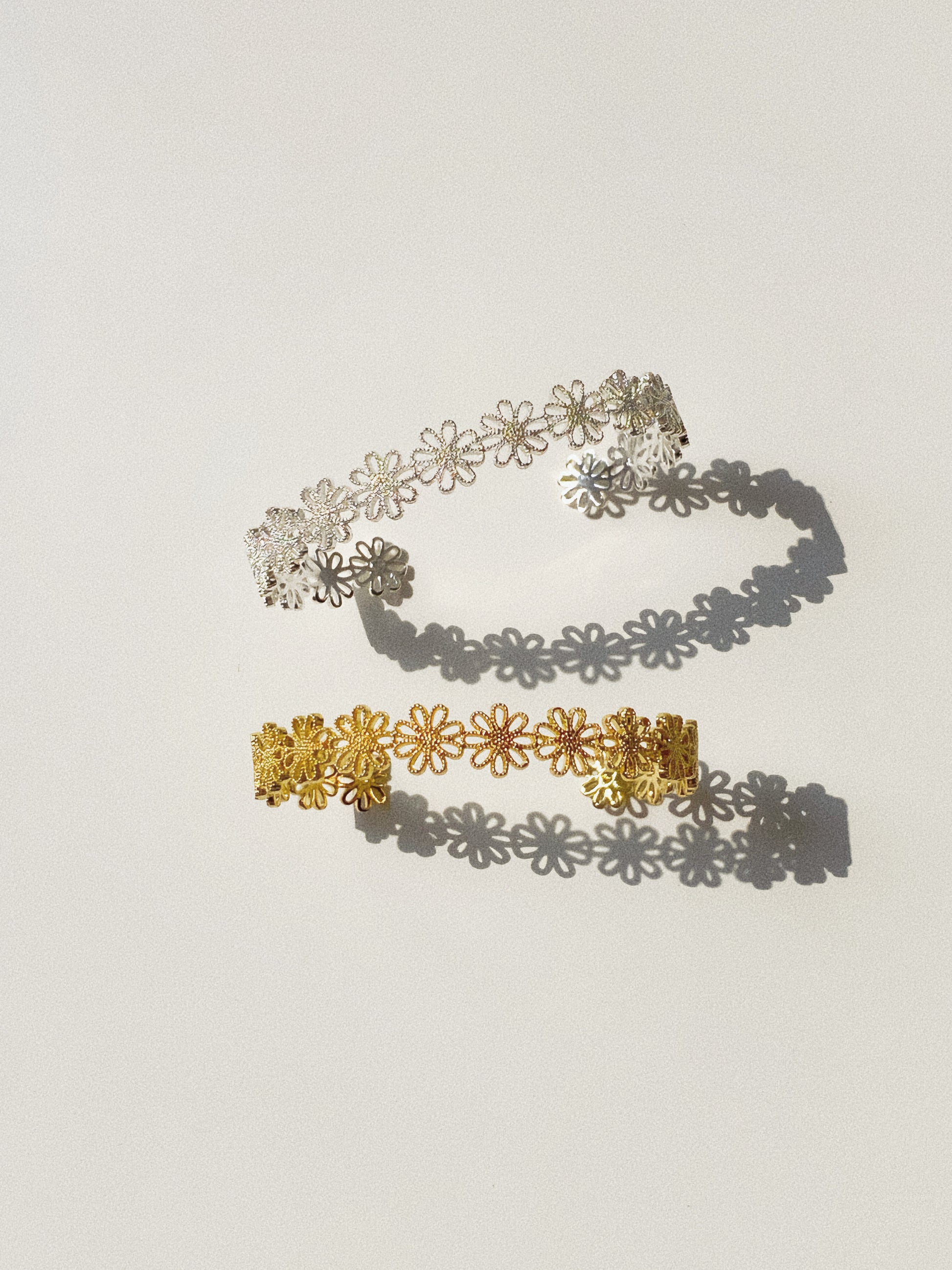 Daisy lace floral open cuff bracelet in gold and silver finishes flat lay with daisy shadow by Deja Vu Jewellery