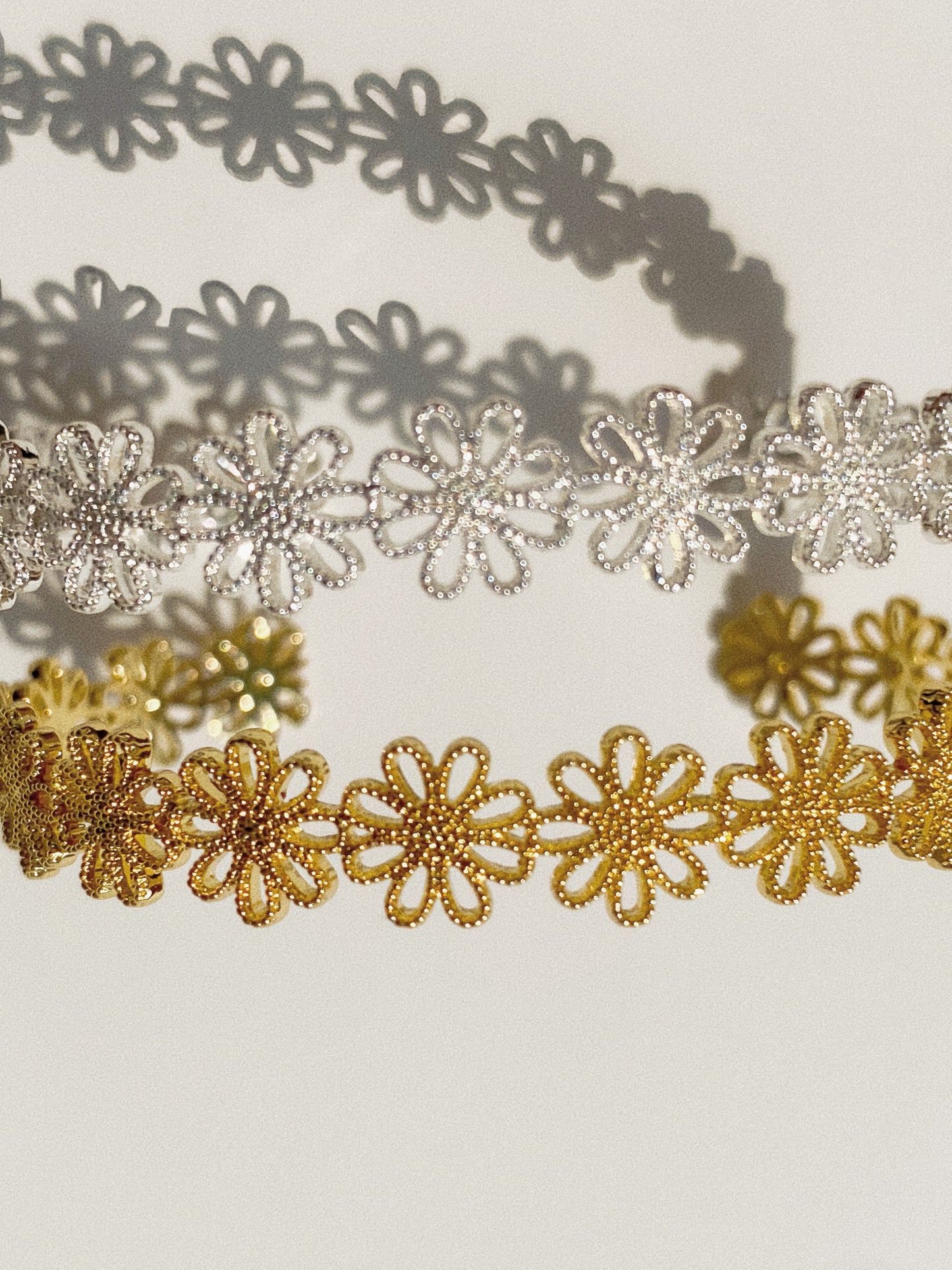 Close-up of gold and silver daisy lace cuff bracelets showing fine floral lacework texture and shadow