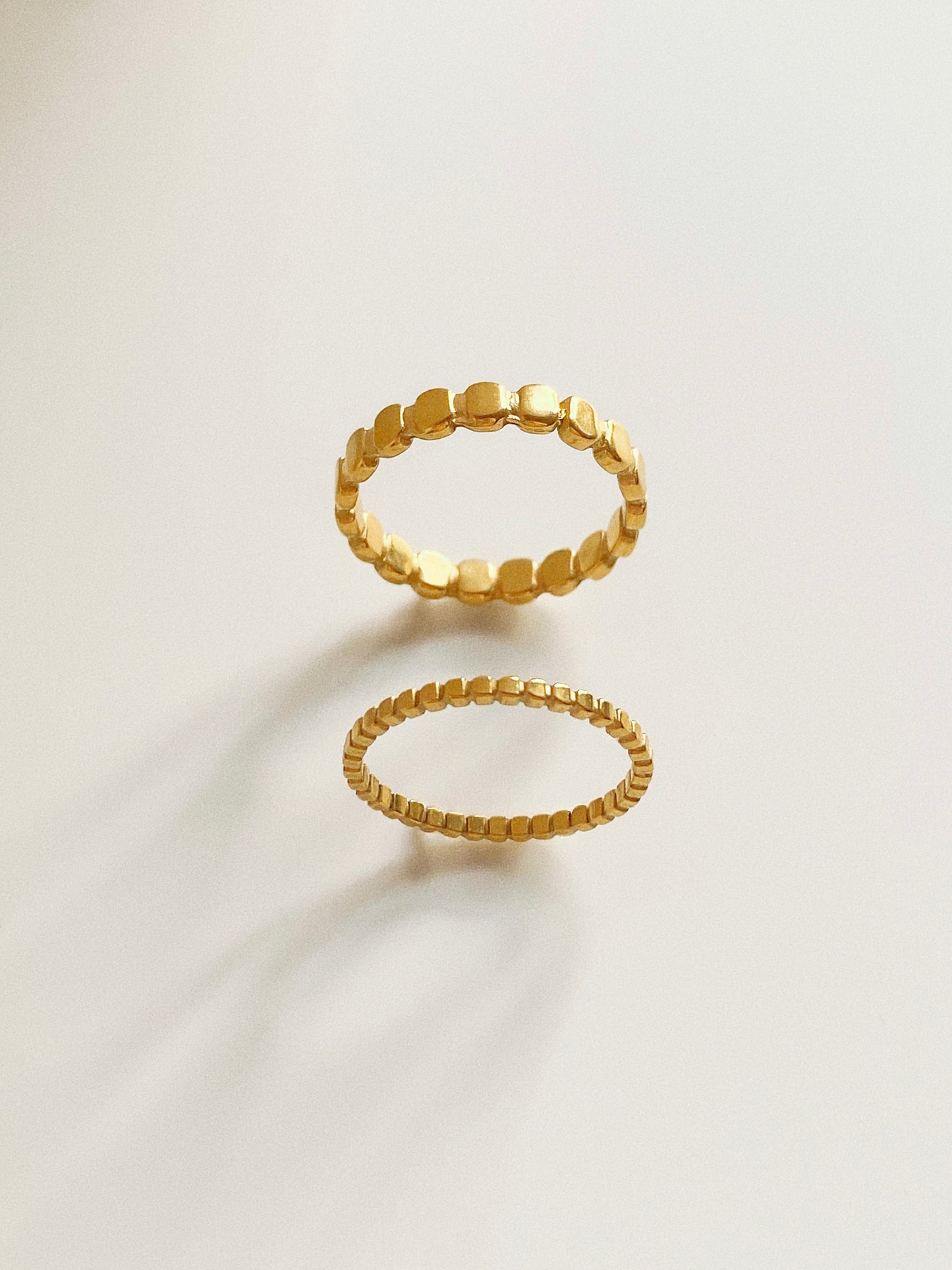  A pair of 18k gold plated titanium steel rings featuring a beaded oval pattern in wide and narrow styles.