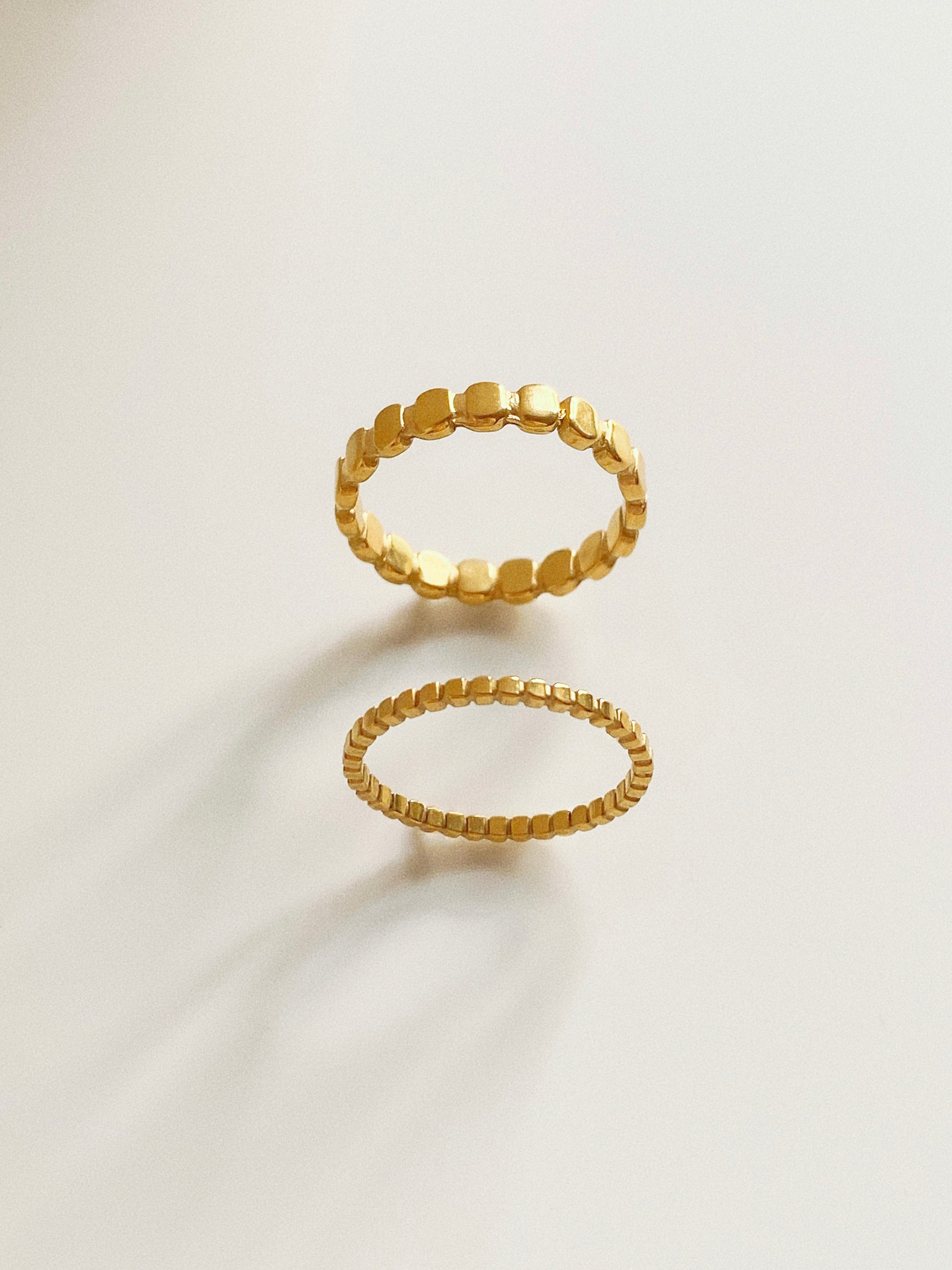  A pair of 18k gold plated titanium steel rings featuring a beaded oval pattern in wide and narrow styles.