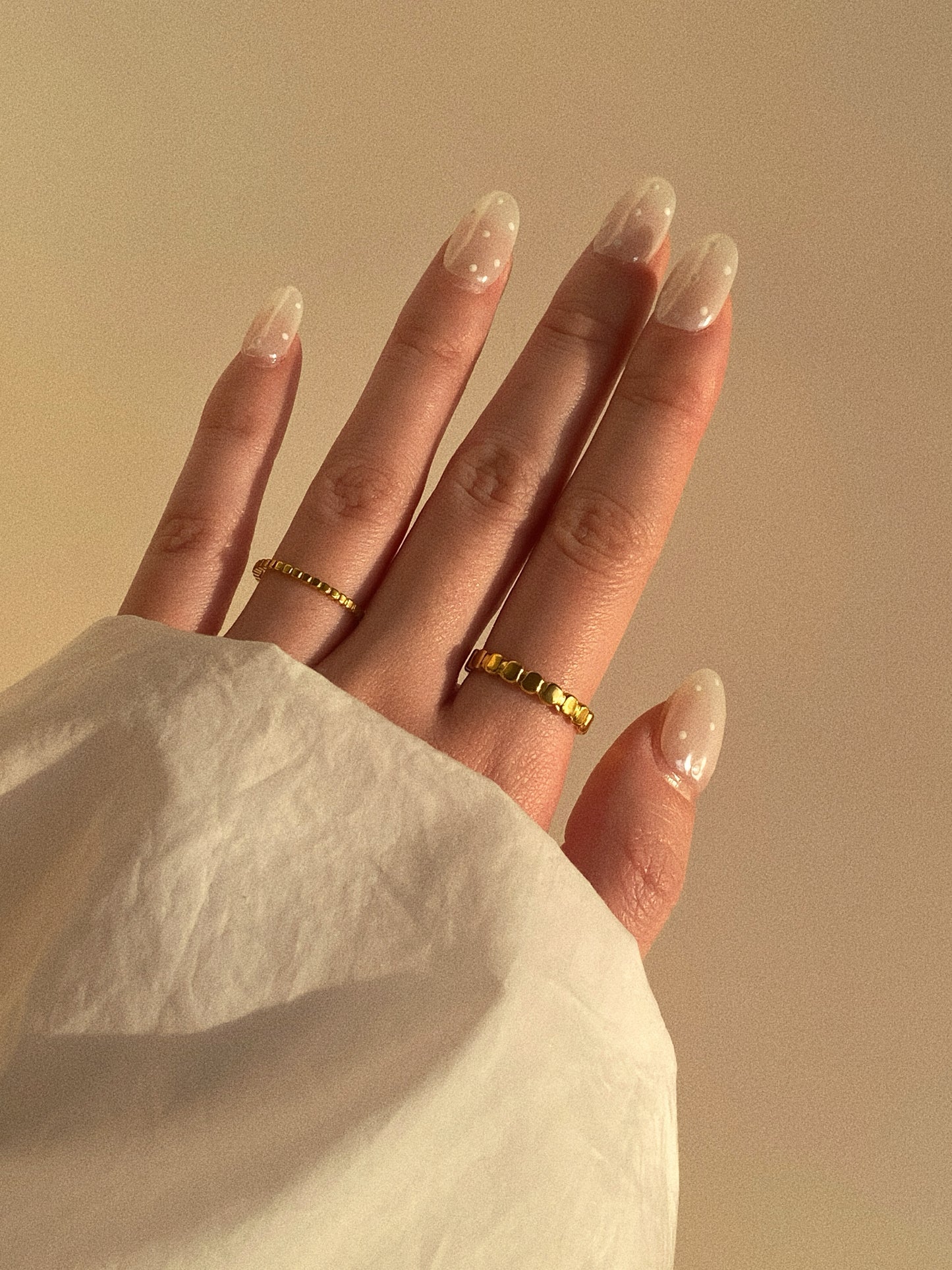 A woman’s hand featuring a modern stack of gold titanium rings against a clean, warm-toned background.