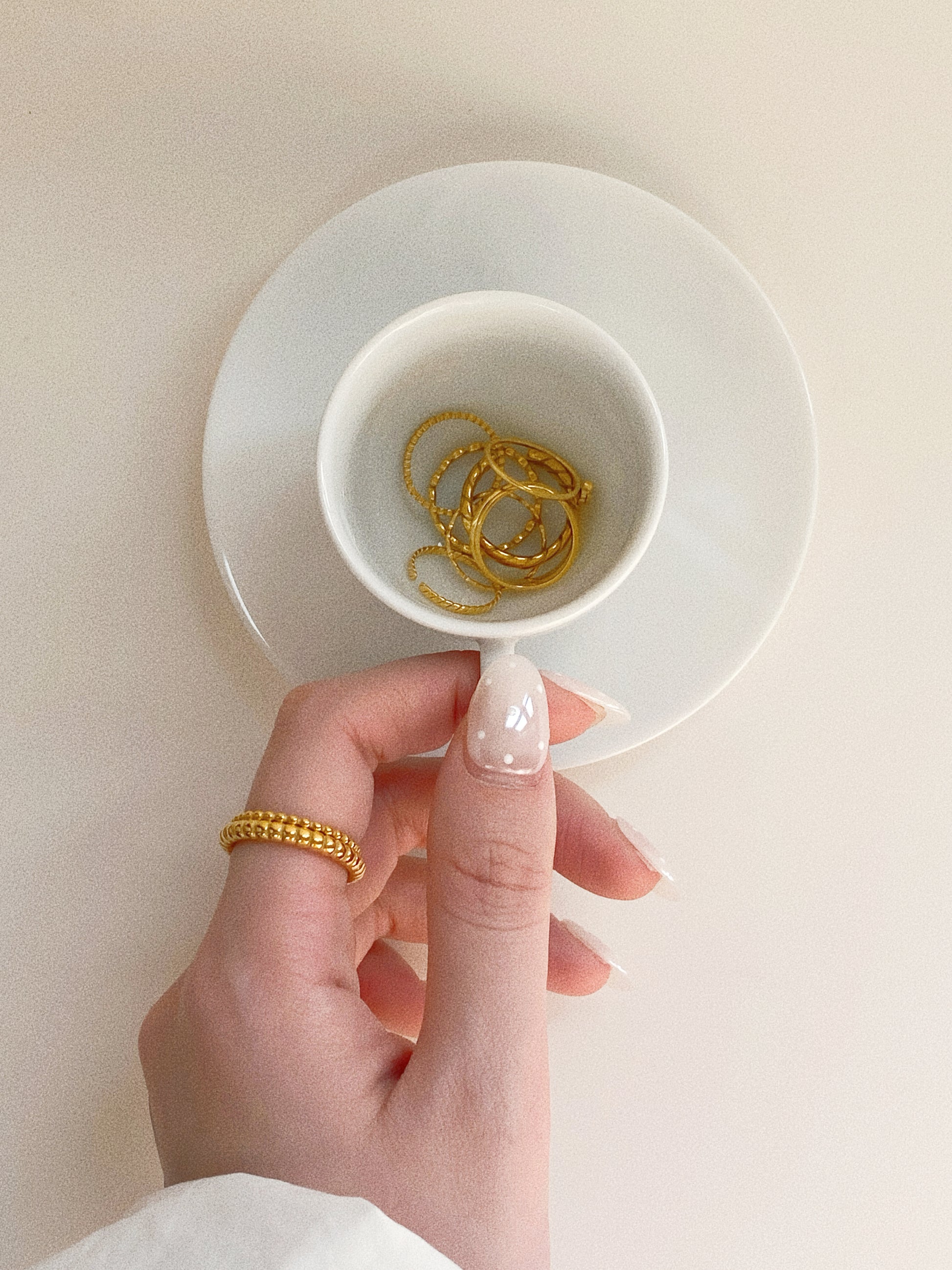Lifestyle shot of a woman's hand featured with a golden ring stack and a cup of coffee.