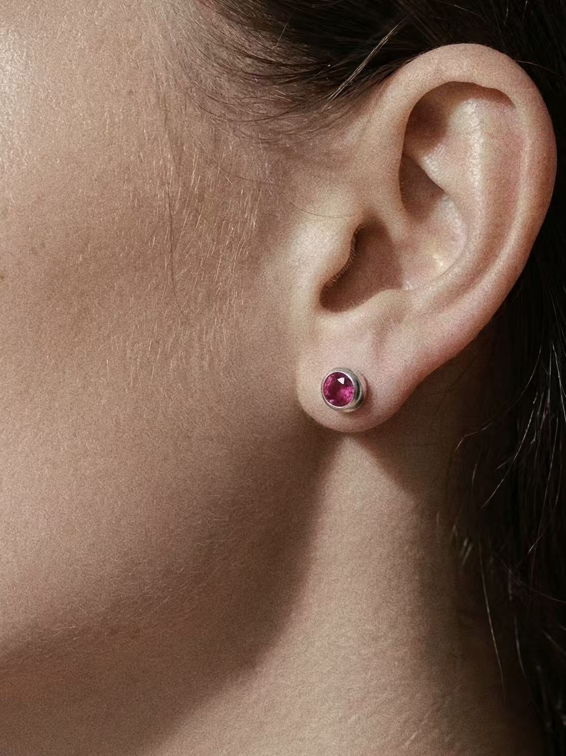 A close-up lifestyle shot of a minimalist natural ruby red gemstone stud earring in a 925 silver bezel setting, perfectly styled for an everyday fashion look.