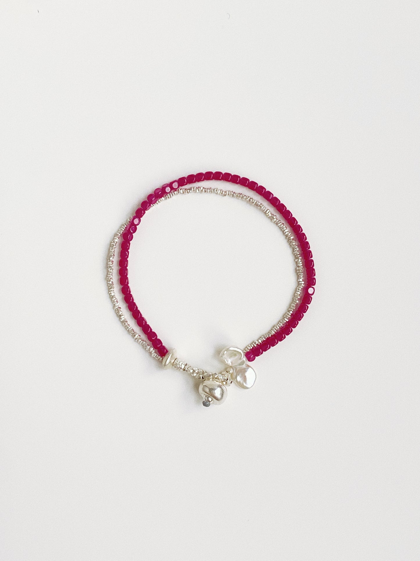 Flat lay view of a double-layer bracelet made of red ruby gemstones, crushed silver beads, and white baroque petal pearls.