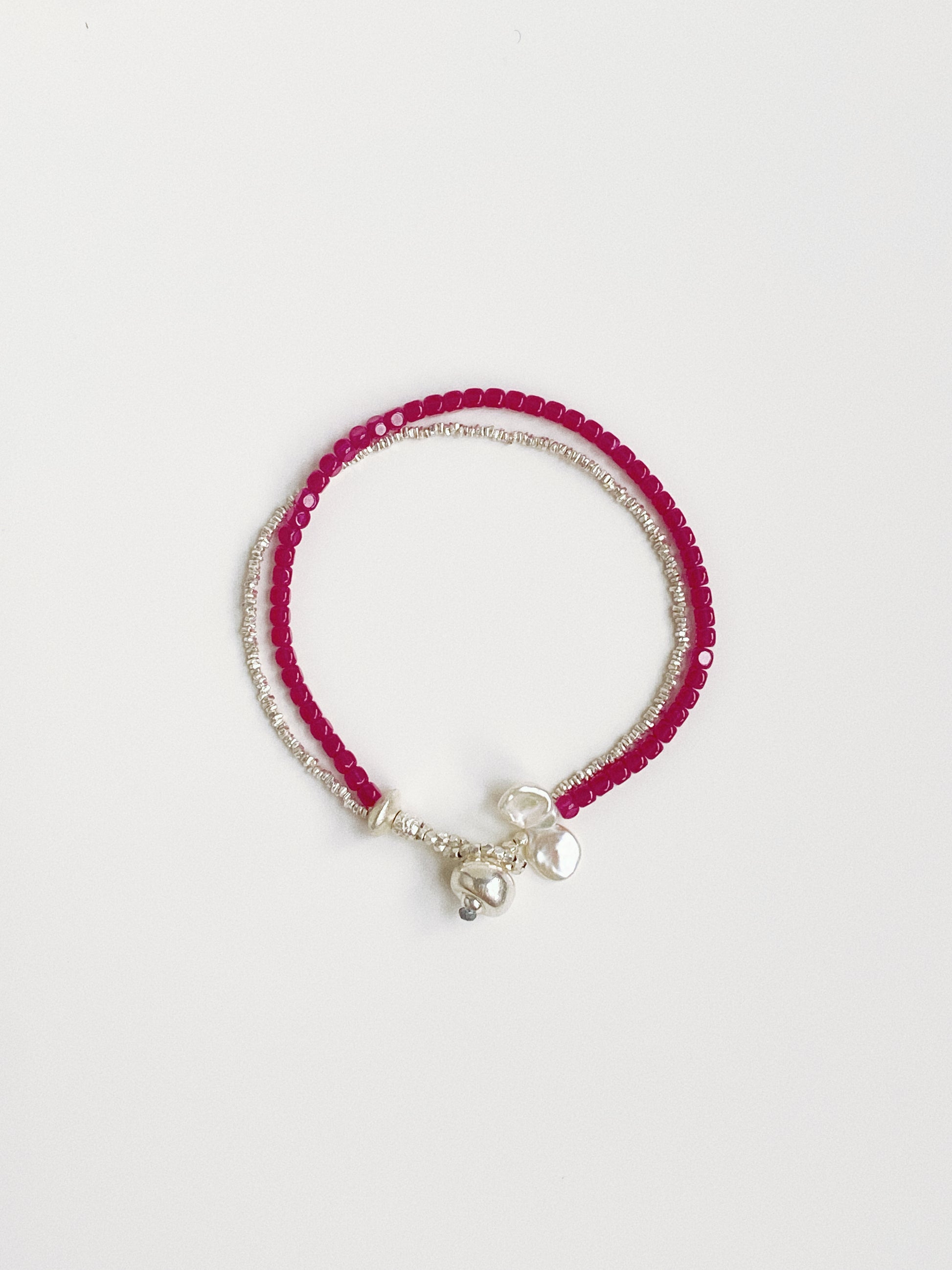 Flat lay view of a double-layer bracelet made of red ruby gemstones, crushed silver beads, and white baroque petal pearls.