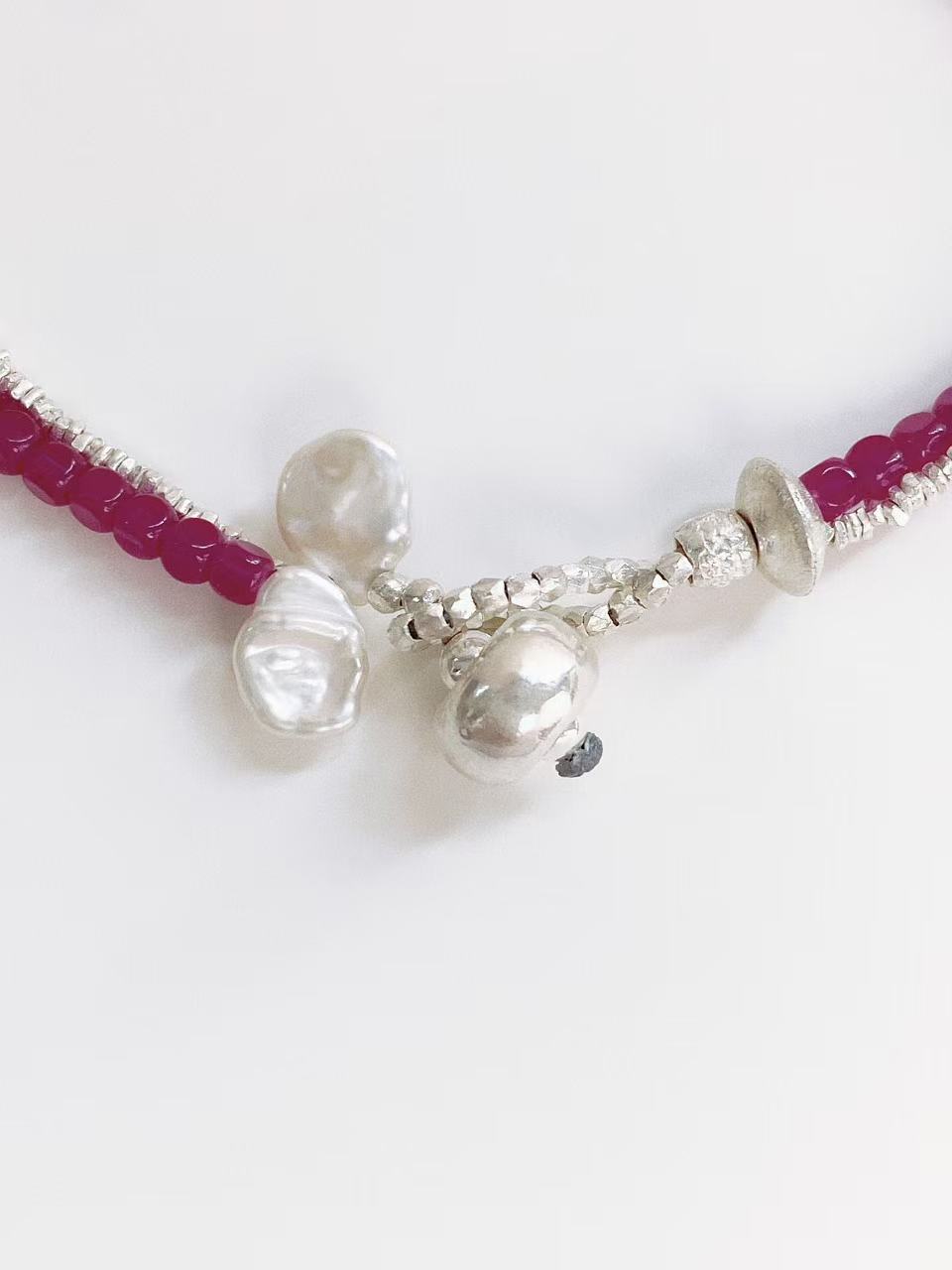 Close-up detail of handcrafted white baroque petal pearls and textured Thai silver charms on a red ruby fashion bracelet by Deja vu Jewellery.