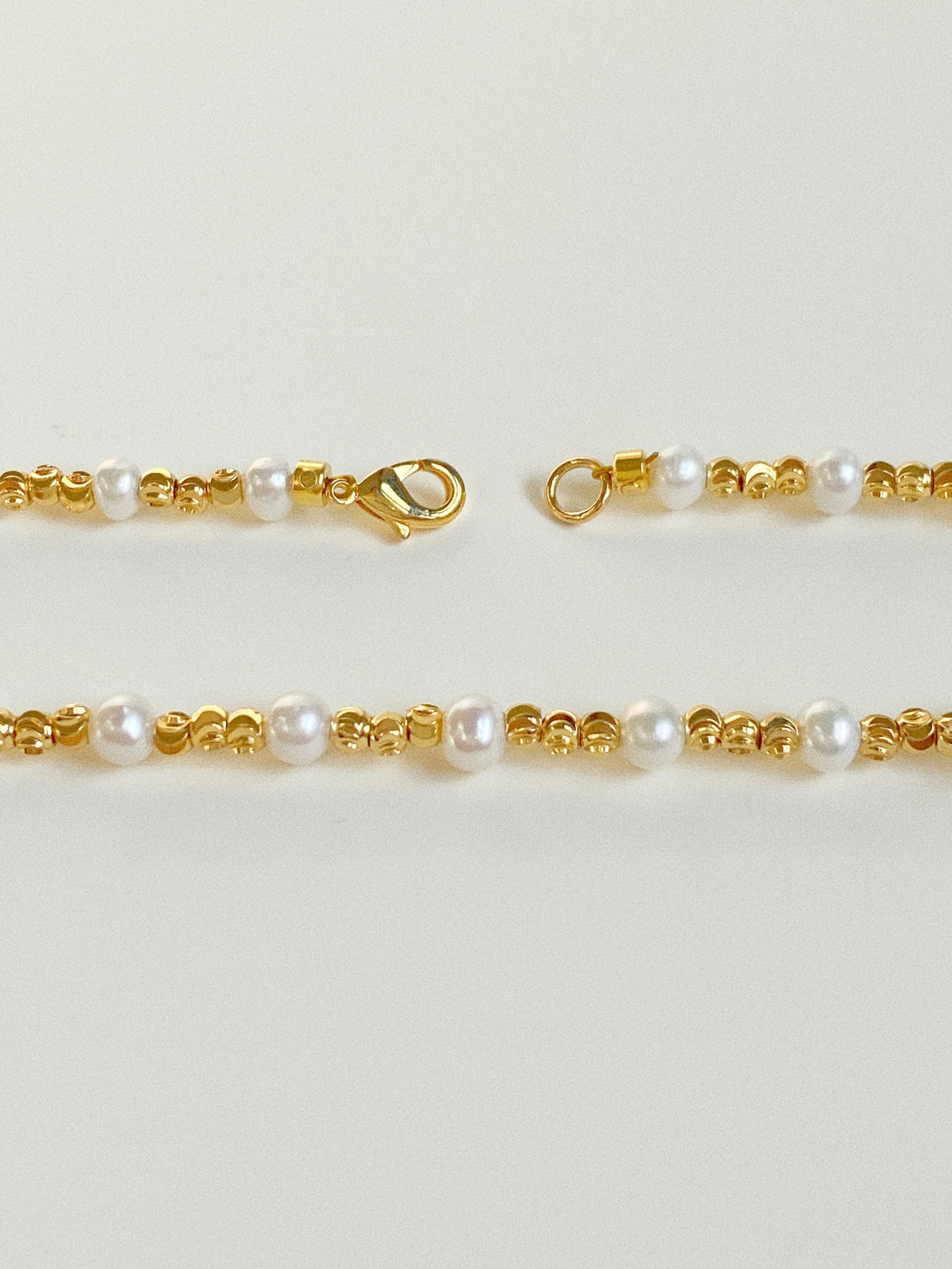 Close-up of waterproof gold lobster clasp and diamond-cut gold beads alternating with natural freshwater pearls
