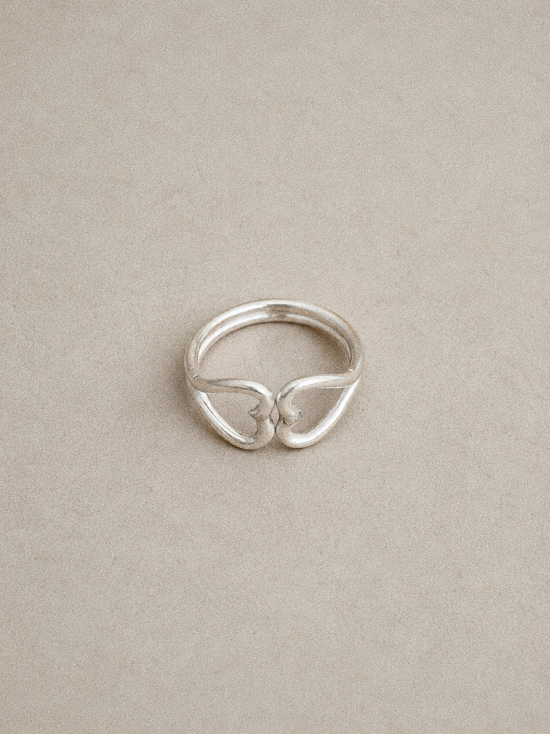 Handmade sterling silver double heart ring lying flat, mirrored open hearts touching tip to tip.