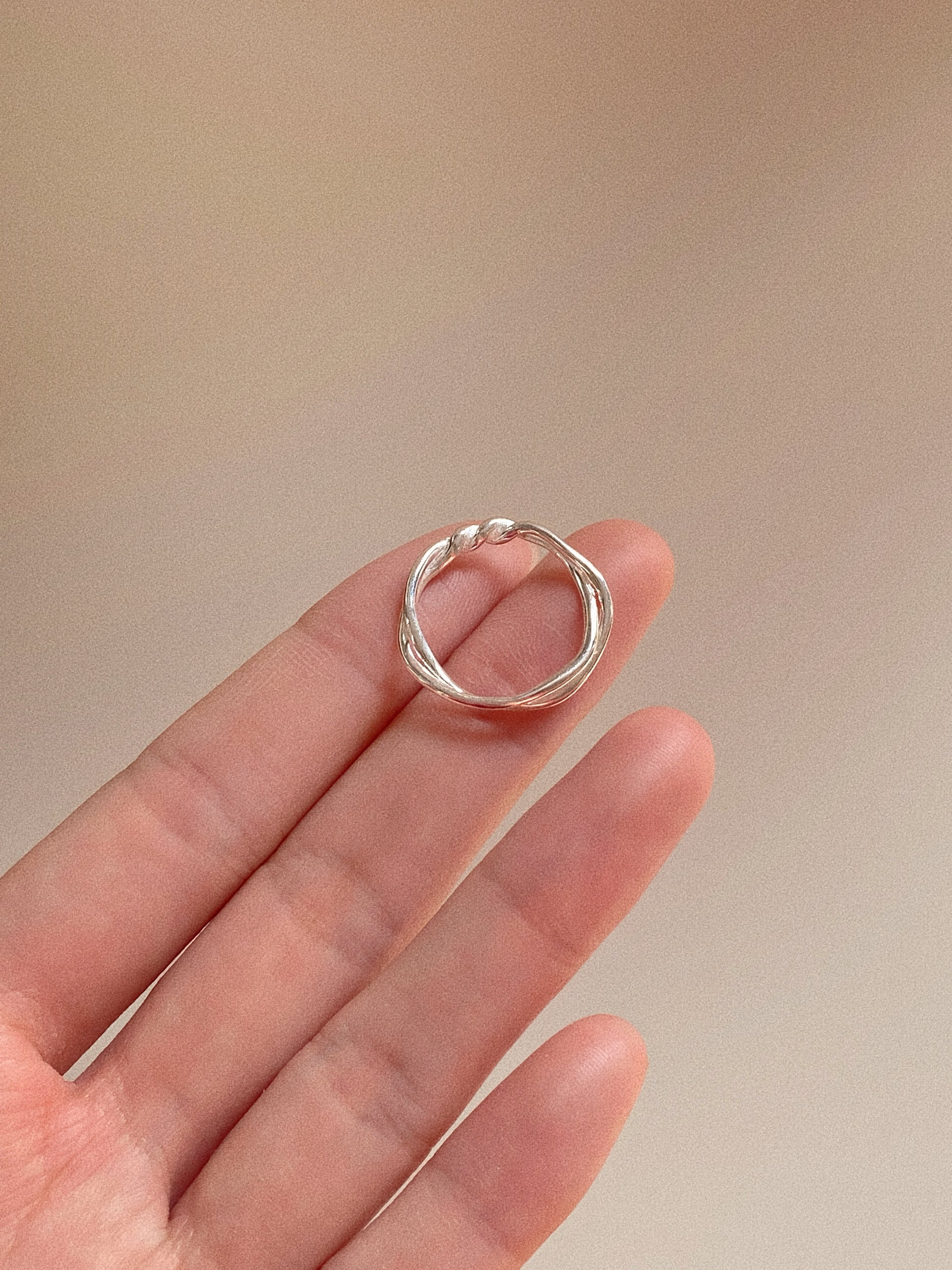 A hand holding the double-layer twisted silver ring to show the detailed craftsmanship and polished finish.
