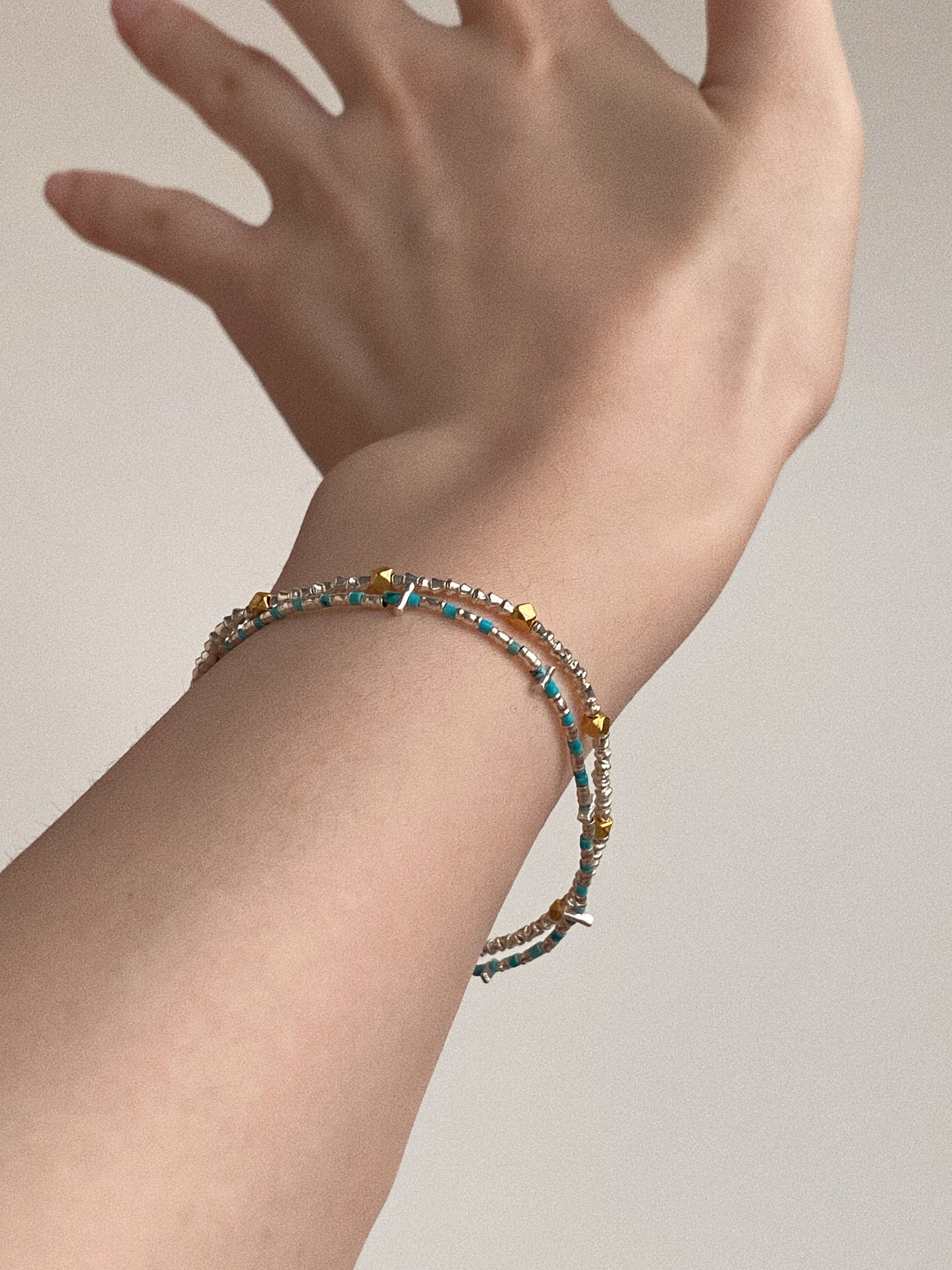 Double-layer natural turquoise bracelet with mixed silver and gold beads styled on a woman's wrist