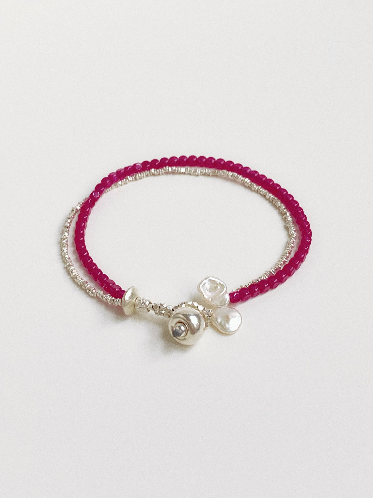 Close up of a handcrafted double-strand bracelet featuring vibrant pink-red ruby beads and textured sterling silver accents.