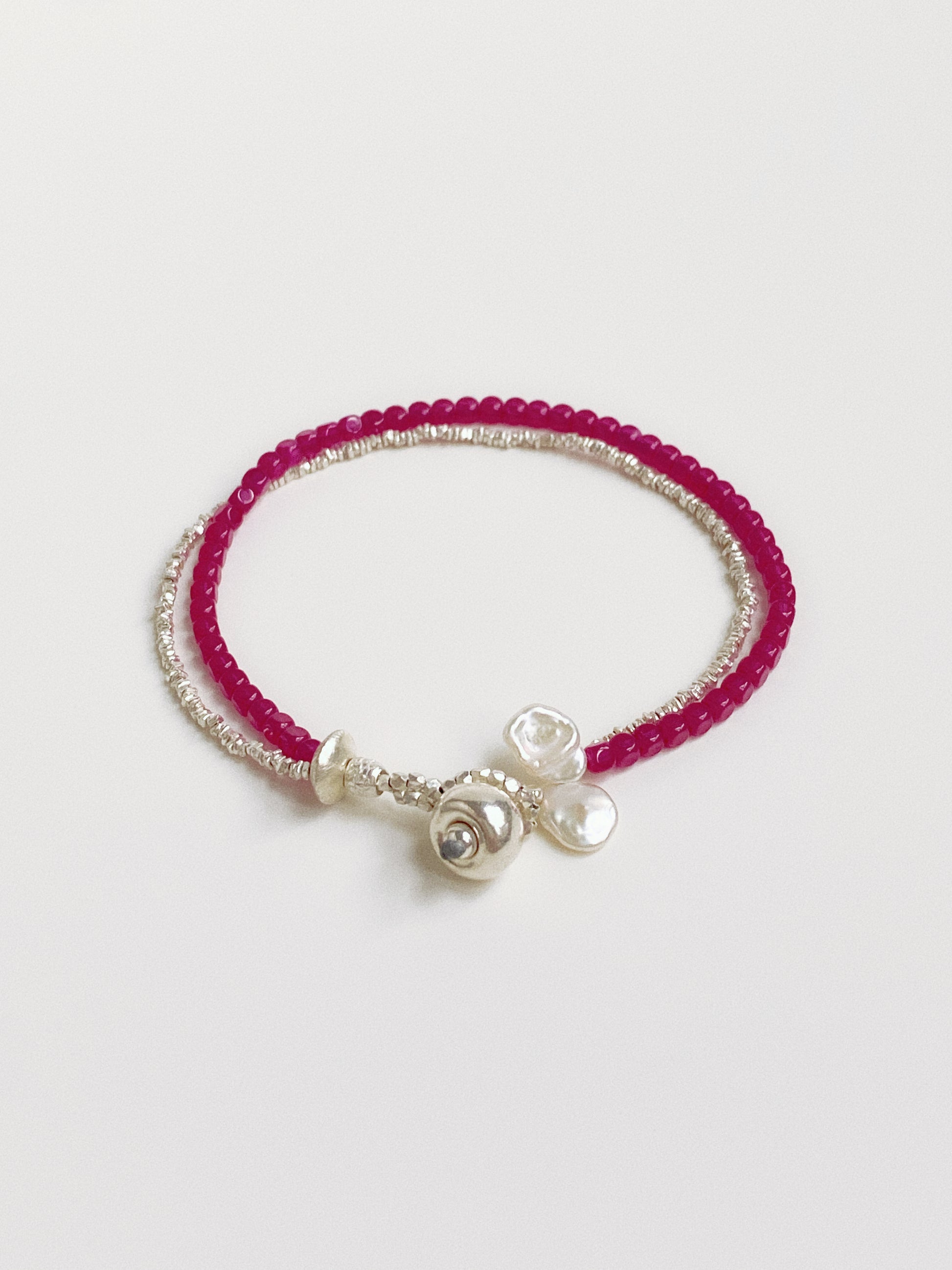 Close up of a handcrafted double-strand bracelet featuring vibrant pink-red ruby beads and textured sterling silver accents.