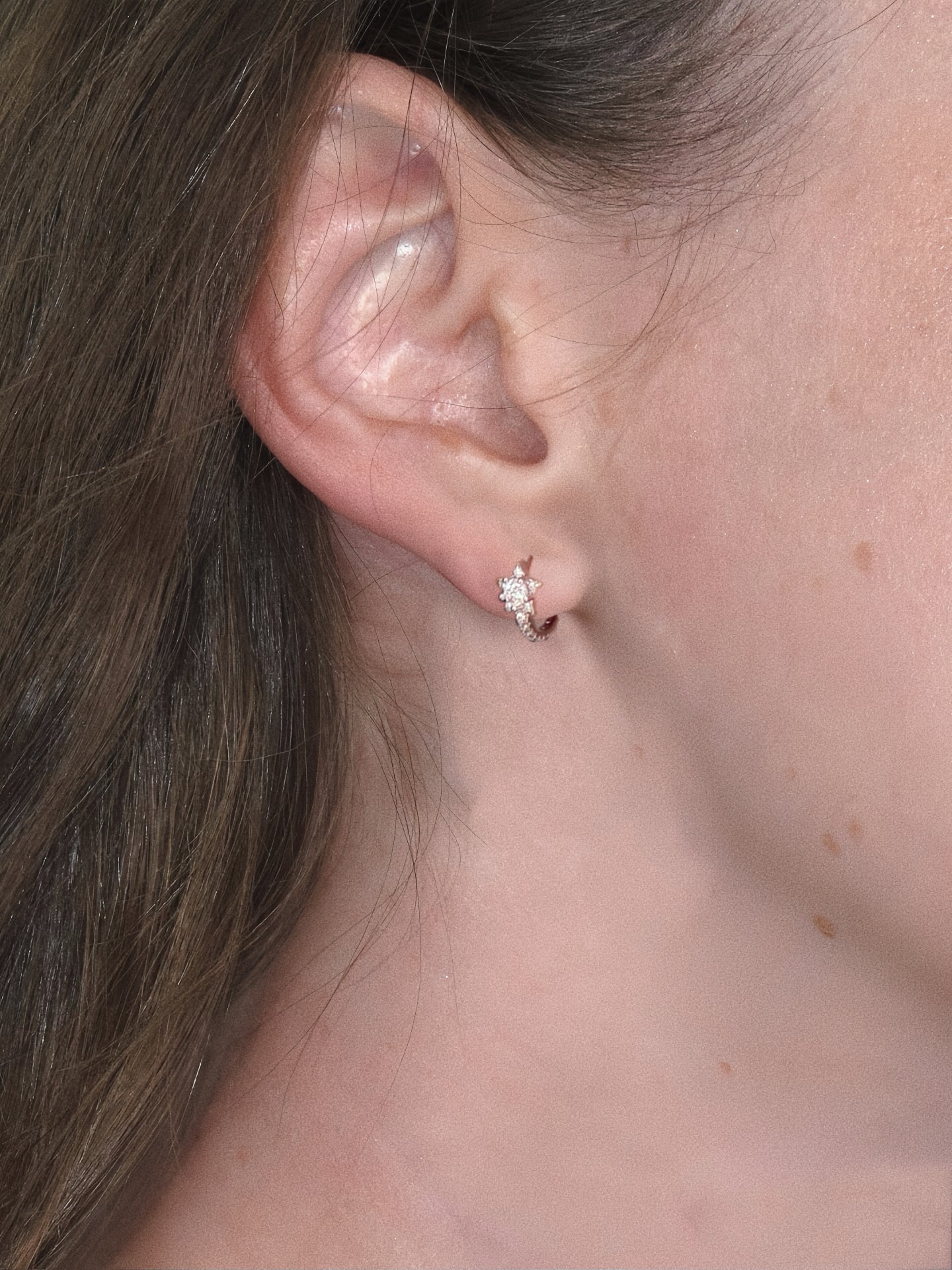 Model wearing silver star huggie earring in first lobe piercing, showing 12.5mm size fit on ear.