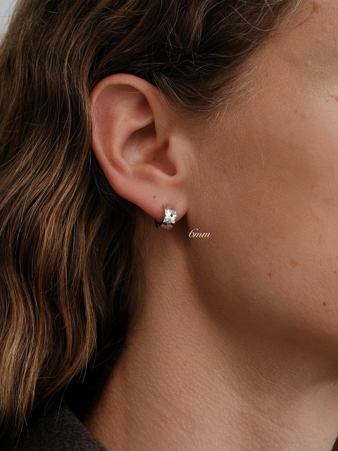 Model wearing 6mm silver huggie hoop in second lobe piercing, demonstrating a snug fit.