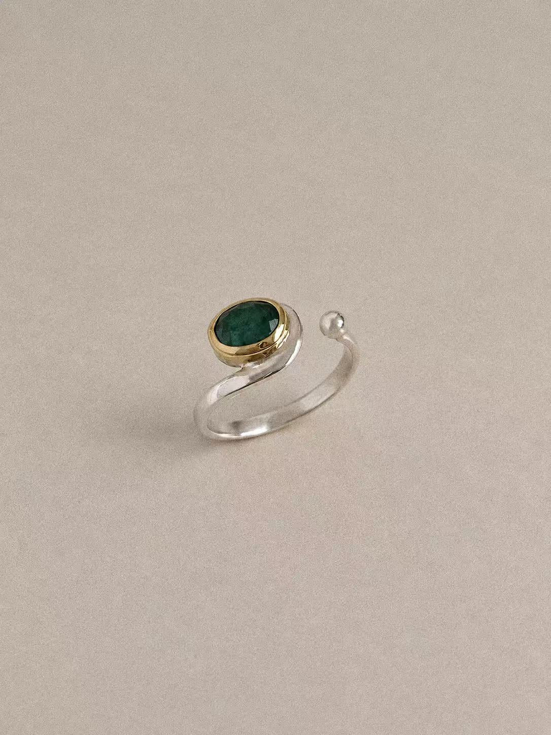 Side view of the emerald ring showing the brass bezel, sweeping silver band and rounded open end