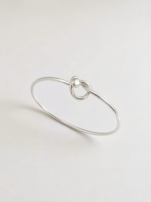 Polished 925 sterling silver love knot bangle with a single sculptural knot and silver ball detail on a soft grey background
