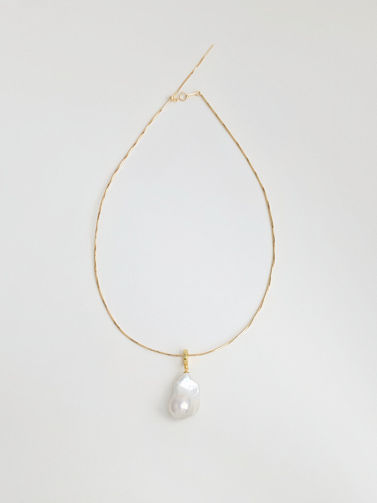 Full flat lay of snake chain choker necklace with natural baroque fishtail freshwater pearl pendant