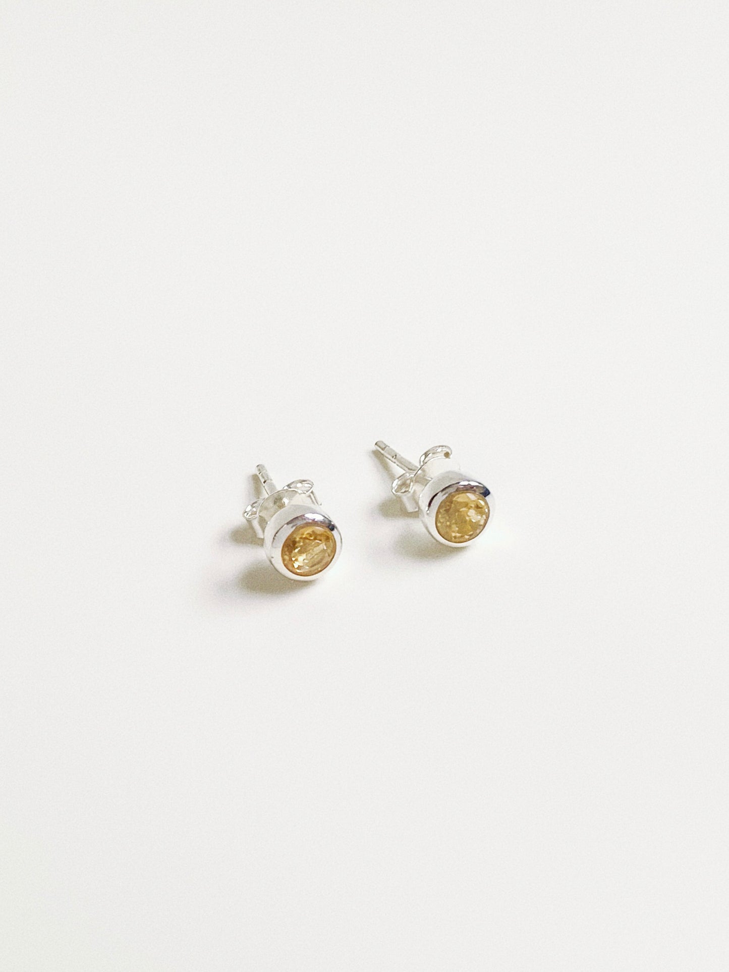 Angled view of sunny yellow citrine studs showing the faceted cut gemstone and snag-free silver bezel.