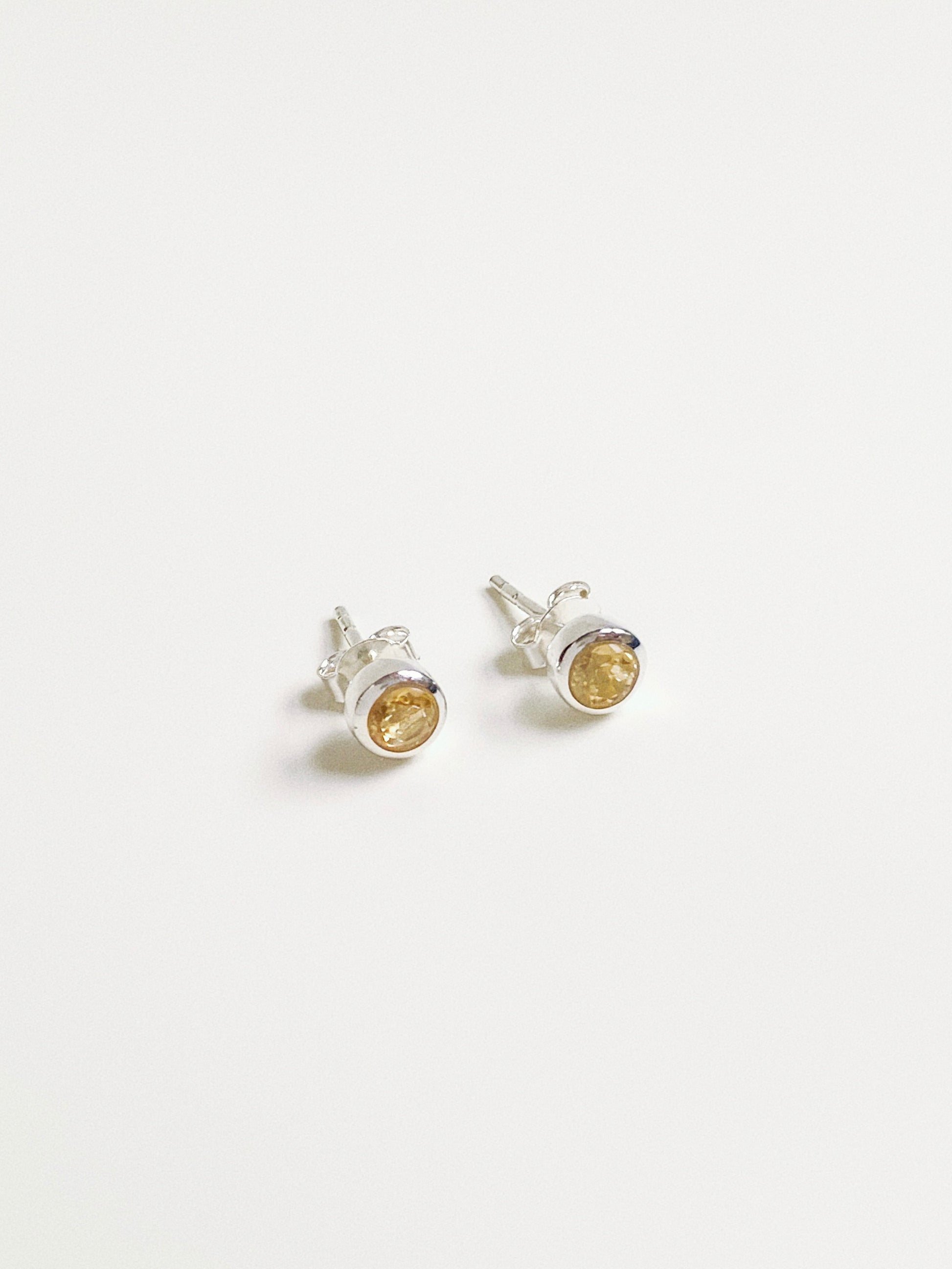 Angled view of sunny yellow citrine studs showing the faceted cut gemstone and snag-free silver bezel.
