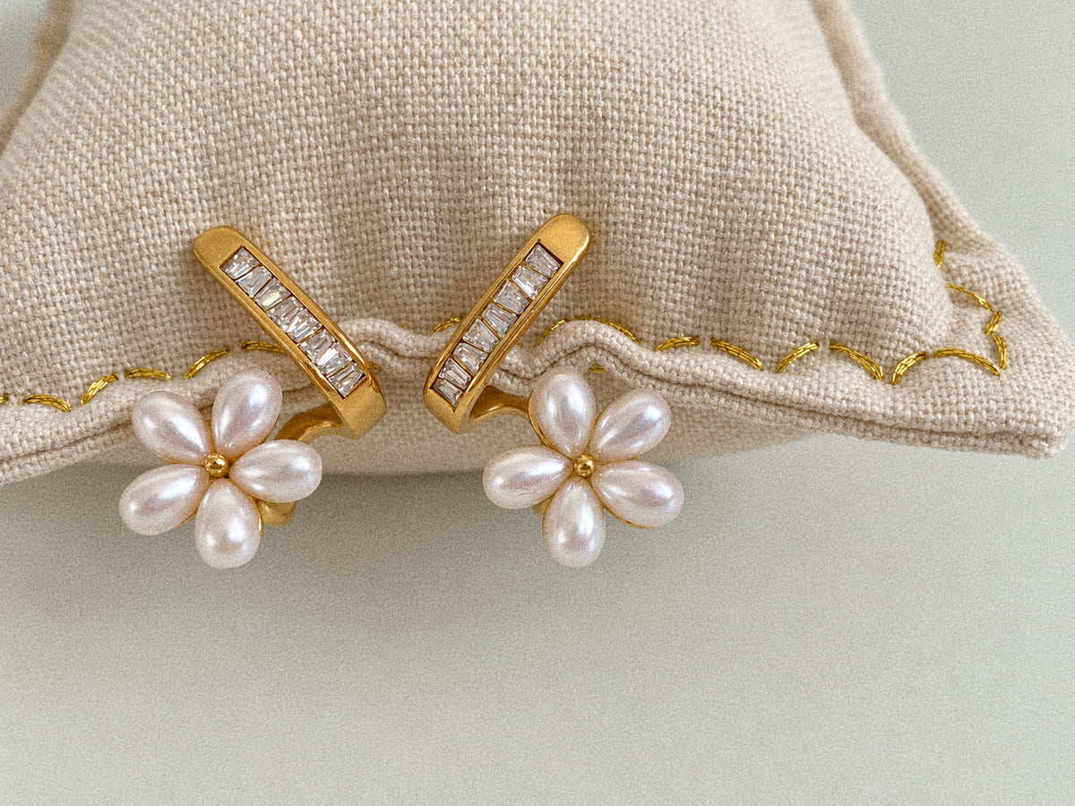Close-up of five white faux pearl petals, gold-tone flower centres and rectangular rhinestones on Fleurette stud earrings.