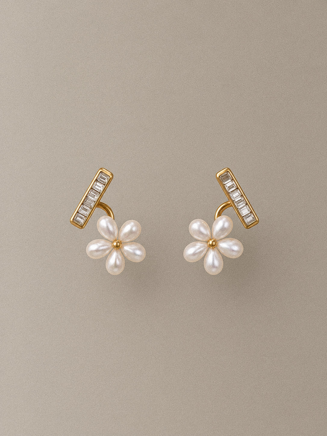 Pair of Fleurette gold-tone flower stud earrings with white faux pearl petals and clear rhinestone bars on a taupe background.